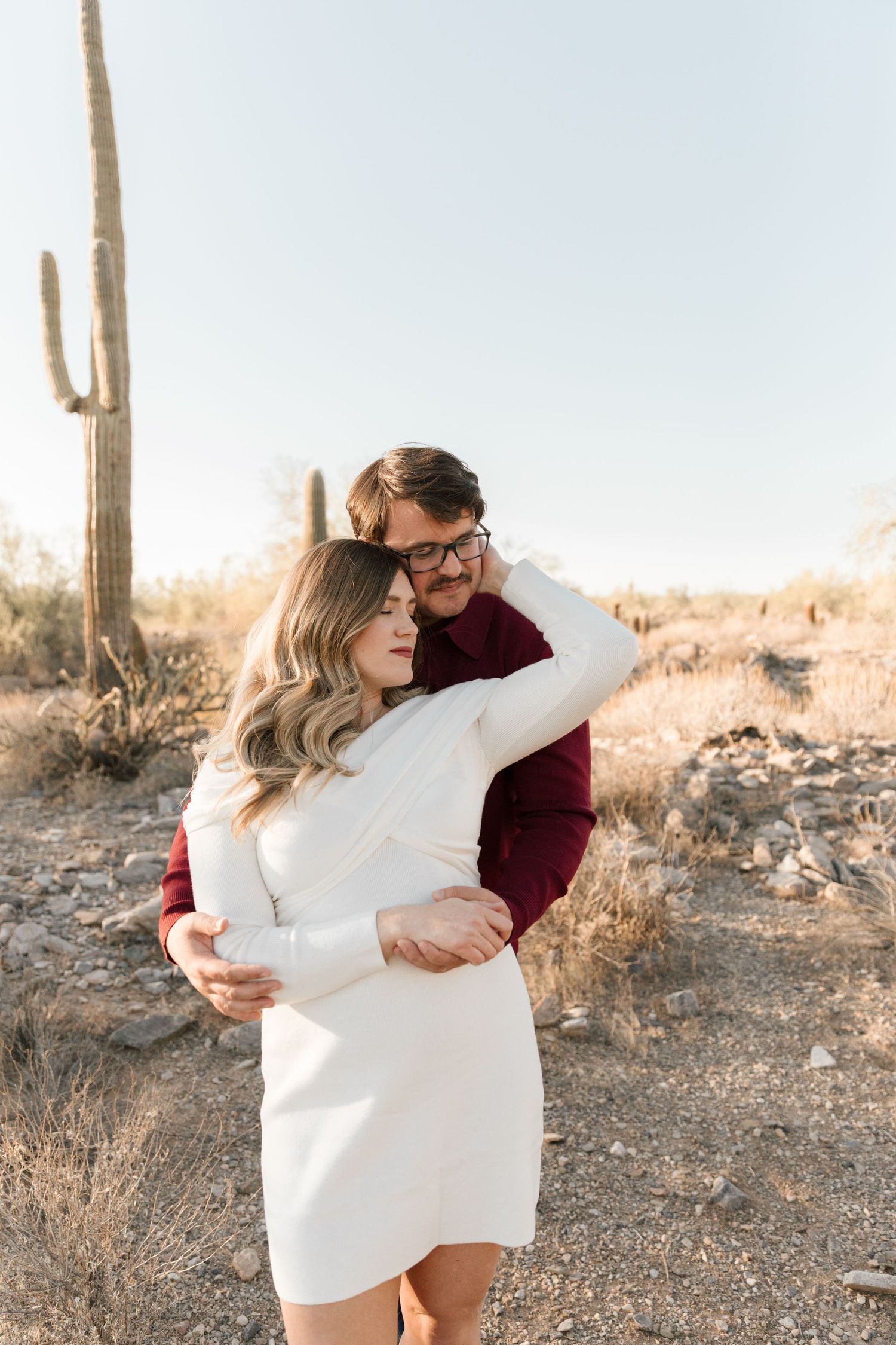 Romantic desert engagement photo with tall saguaro cactus in background at sunset.