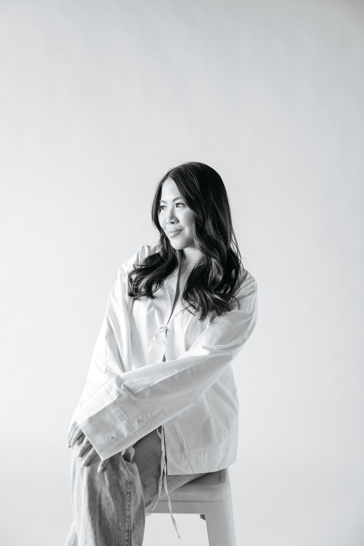 Professional studio portrait of a woman wearing a white button-up shirt against a light background.