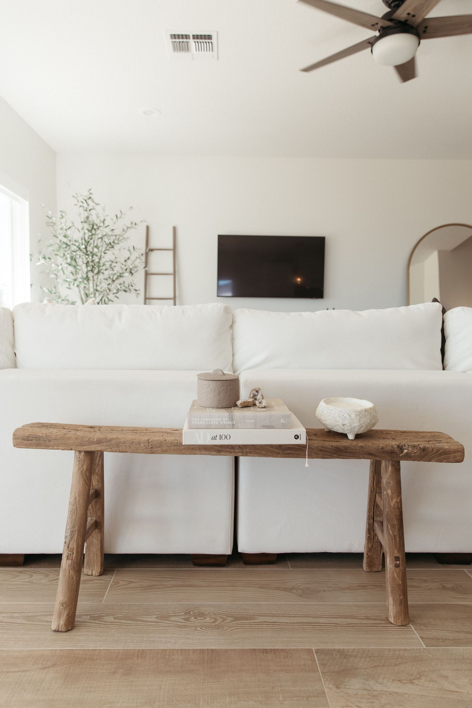 Minimalist living room with white sectional sofa and rustic wooden bench table.