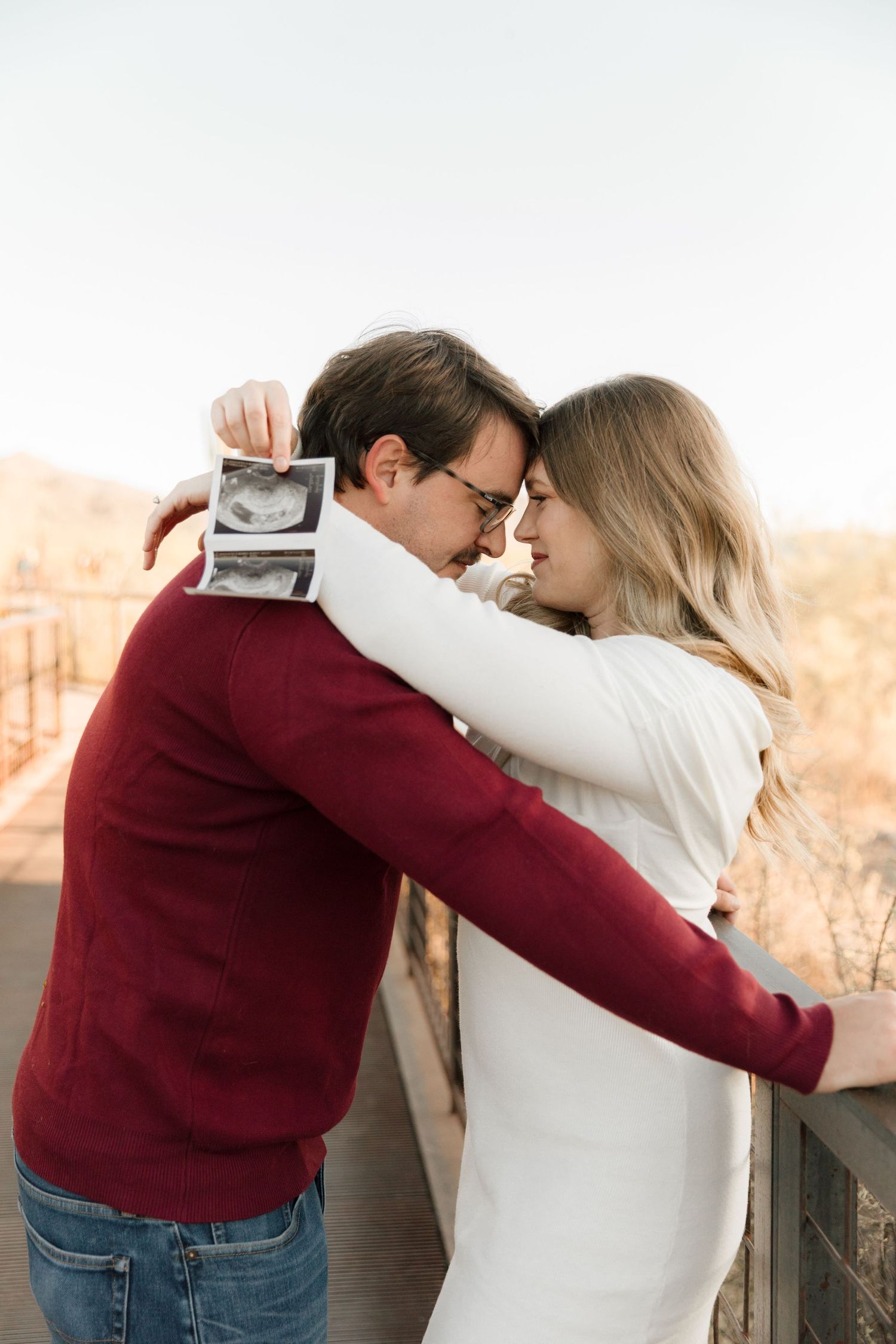 Couple sharing intimate moment while holding ultrasound photo against autumn backdrop.