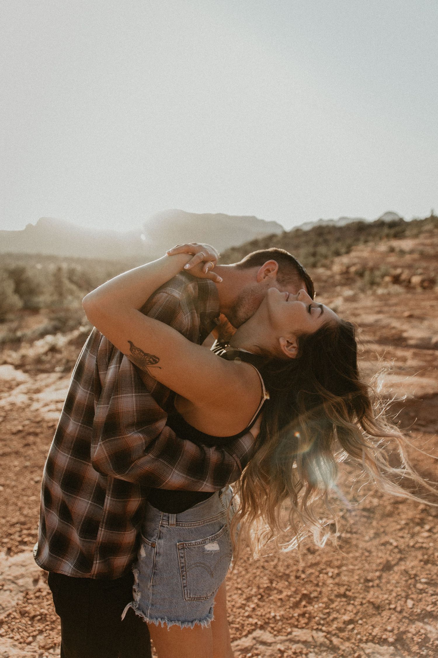 Couple sharing a romantic moment against a desert mountain backdrop at sunset.