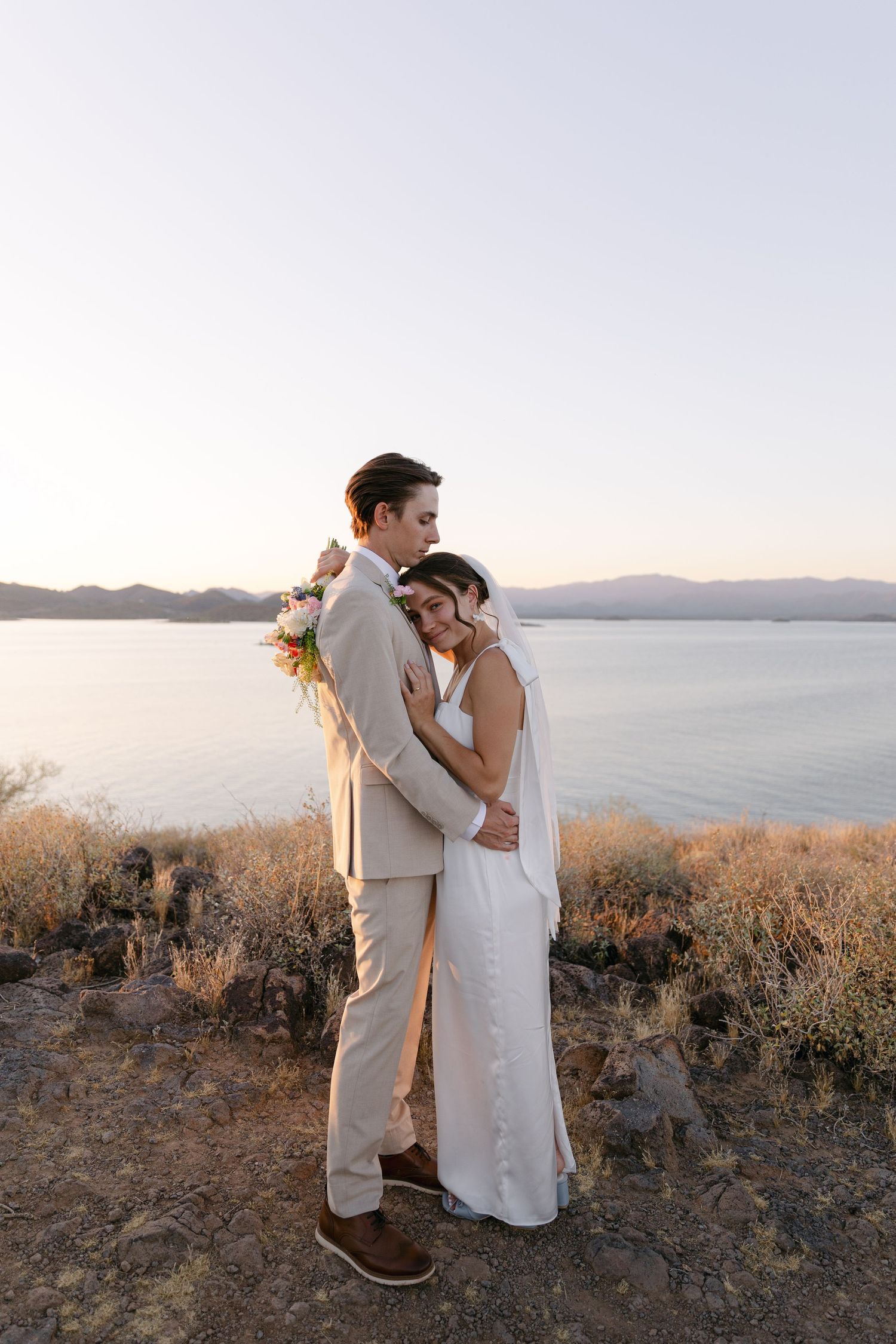 A romantic sunset wedding photo overlooking a serene lake with mountains in the background.
