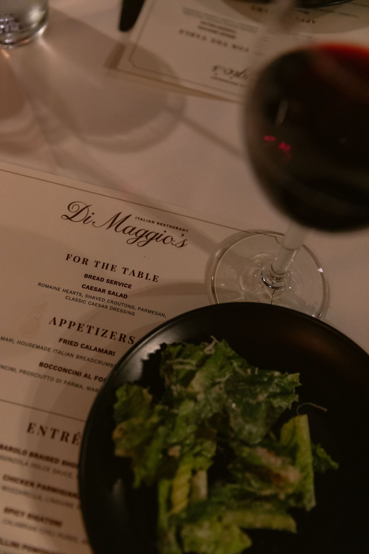 Restaurant menu for Di Maggio's with a salad and wine glass visible on the table.