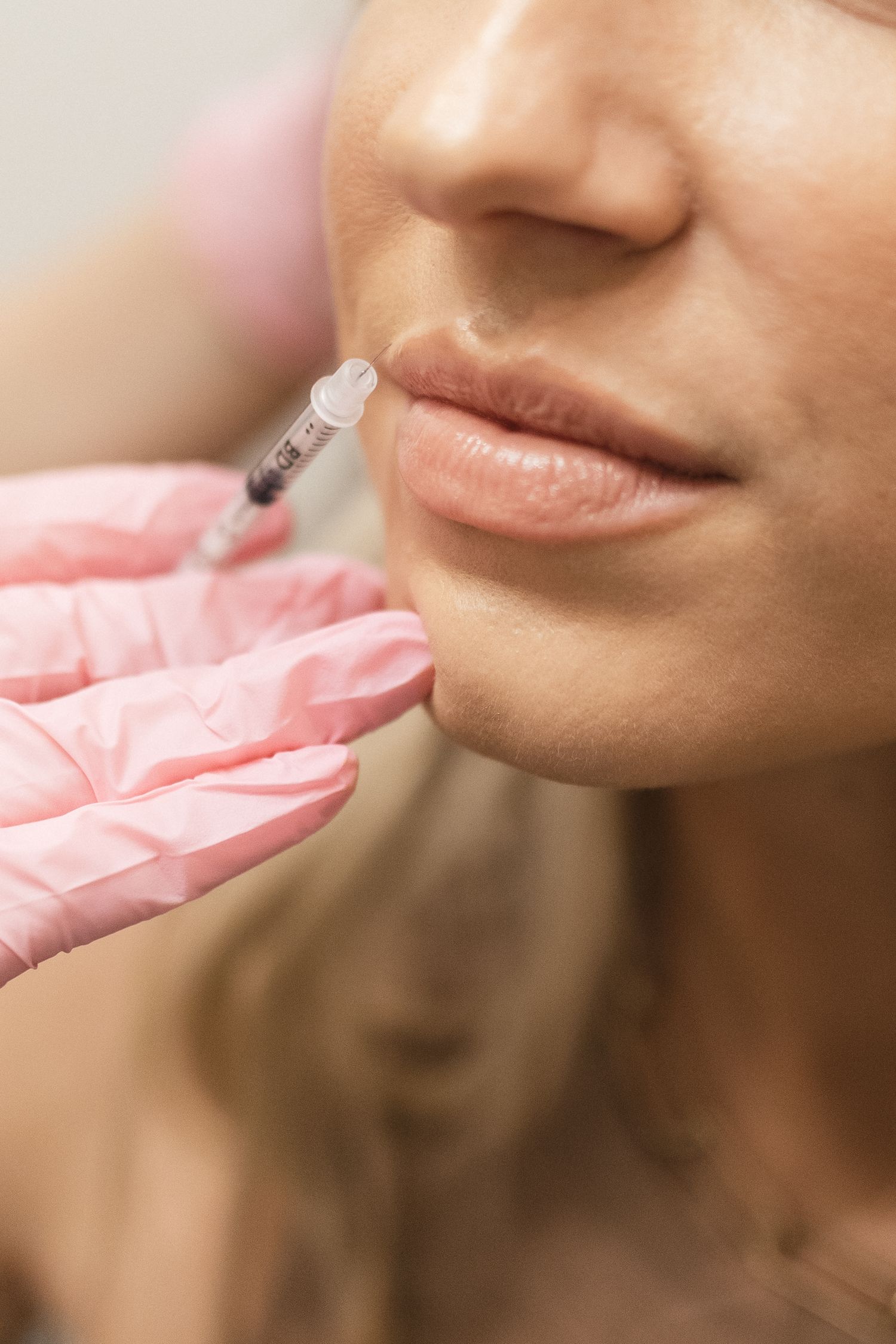 A close-up view of lips receiving a dermal filler injection with gloved hands holding a syringe.