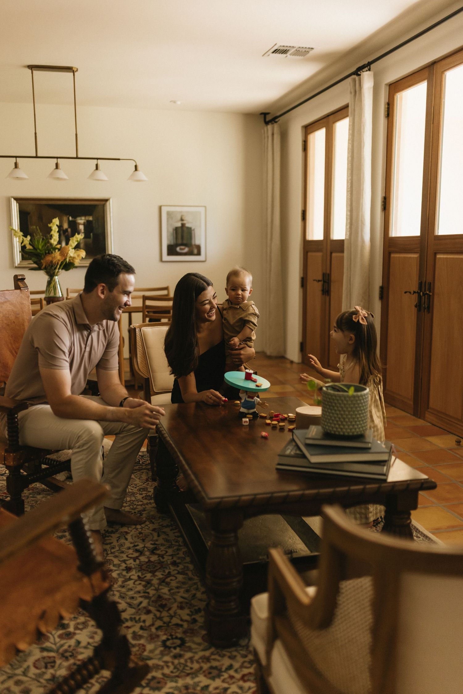 Family of four enjoying playtime together in a warm, cozy living room with wooden furniture and natural light.