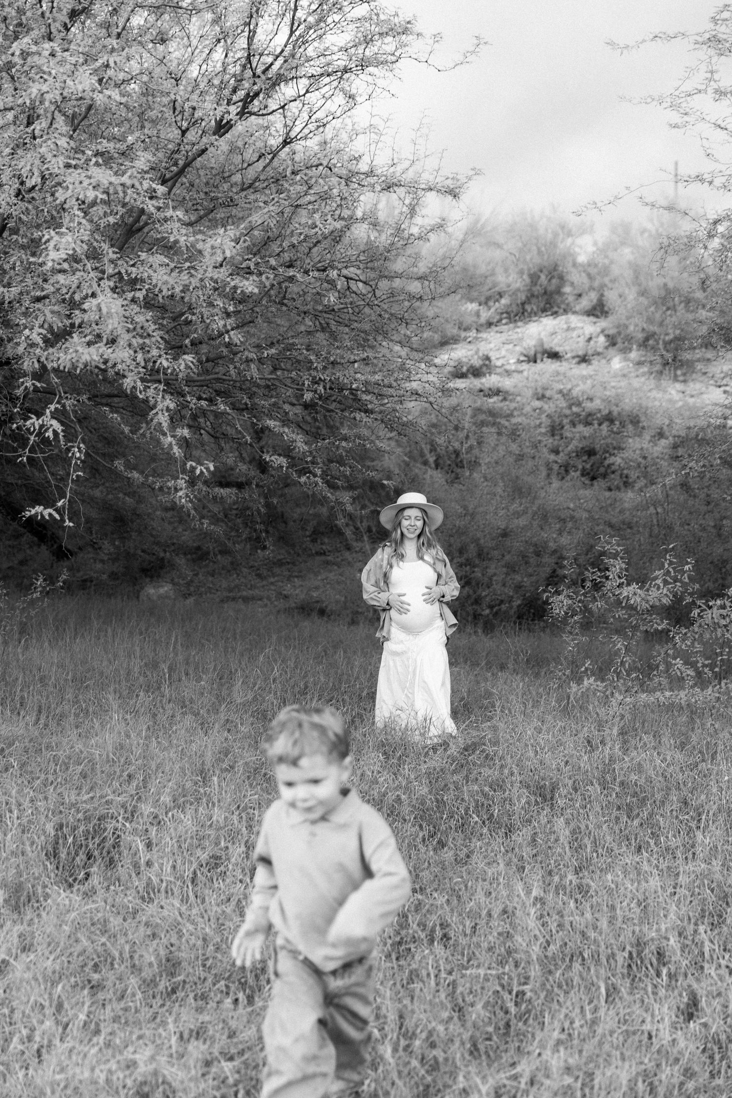 A black and white vintage photograph showing people standing in a grassy meadow surrounded by trees.