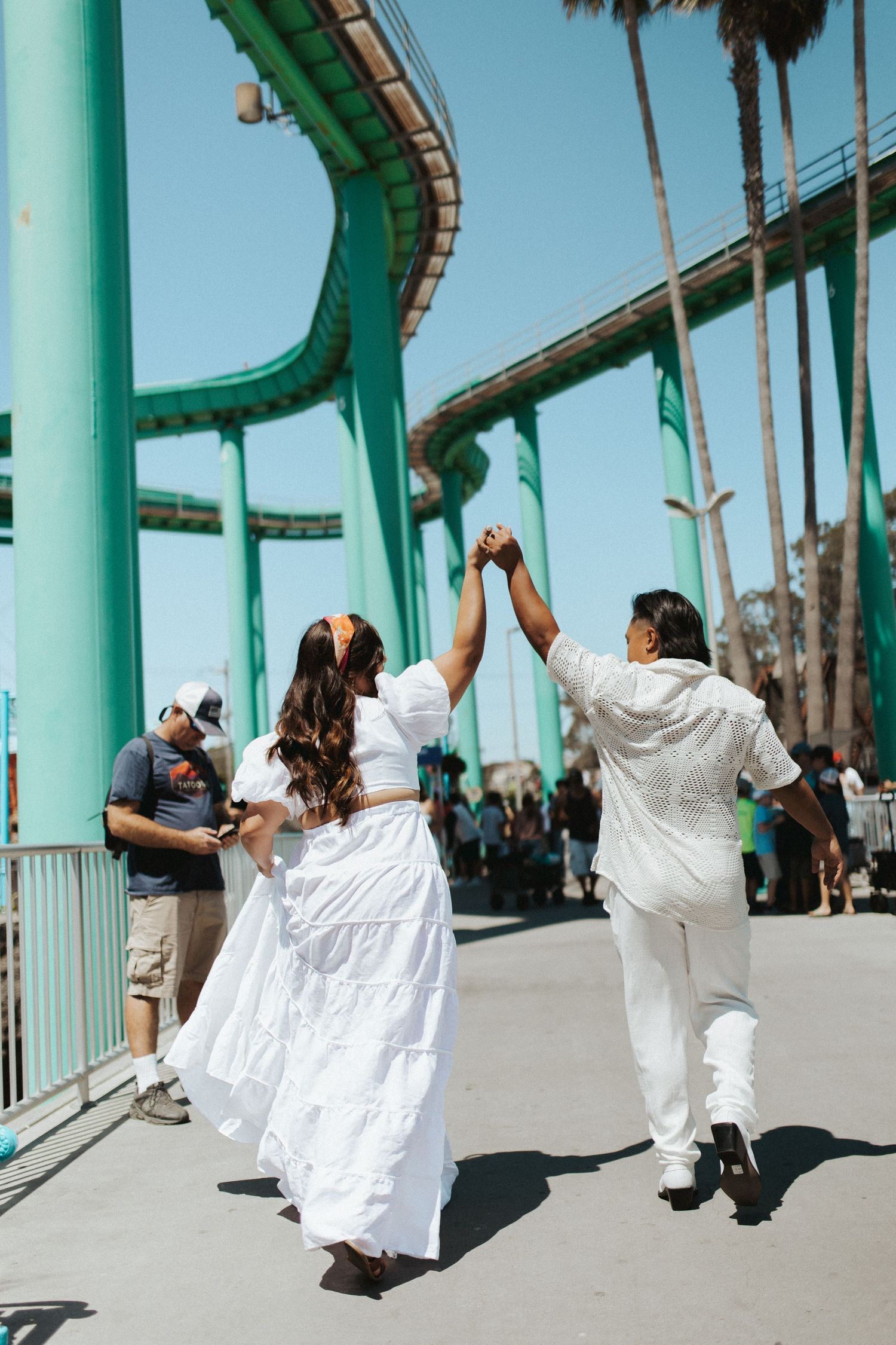 Couple in white clothing dancing together near turquoise amusement park rides.
