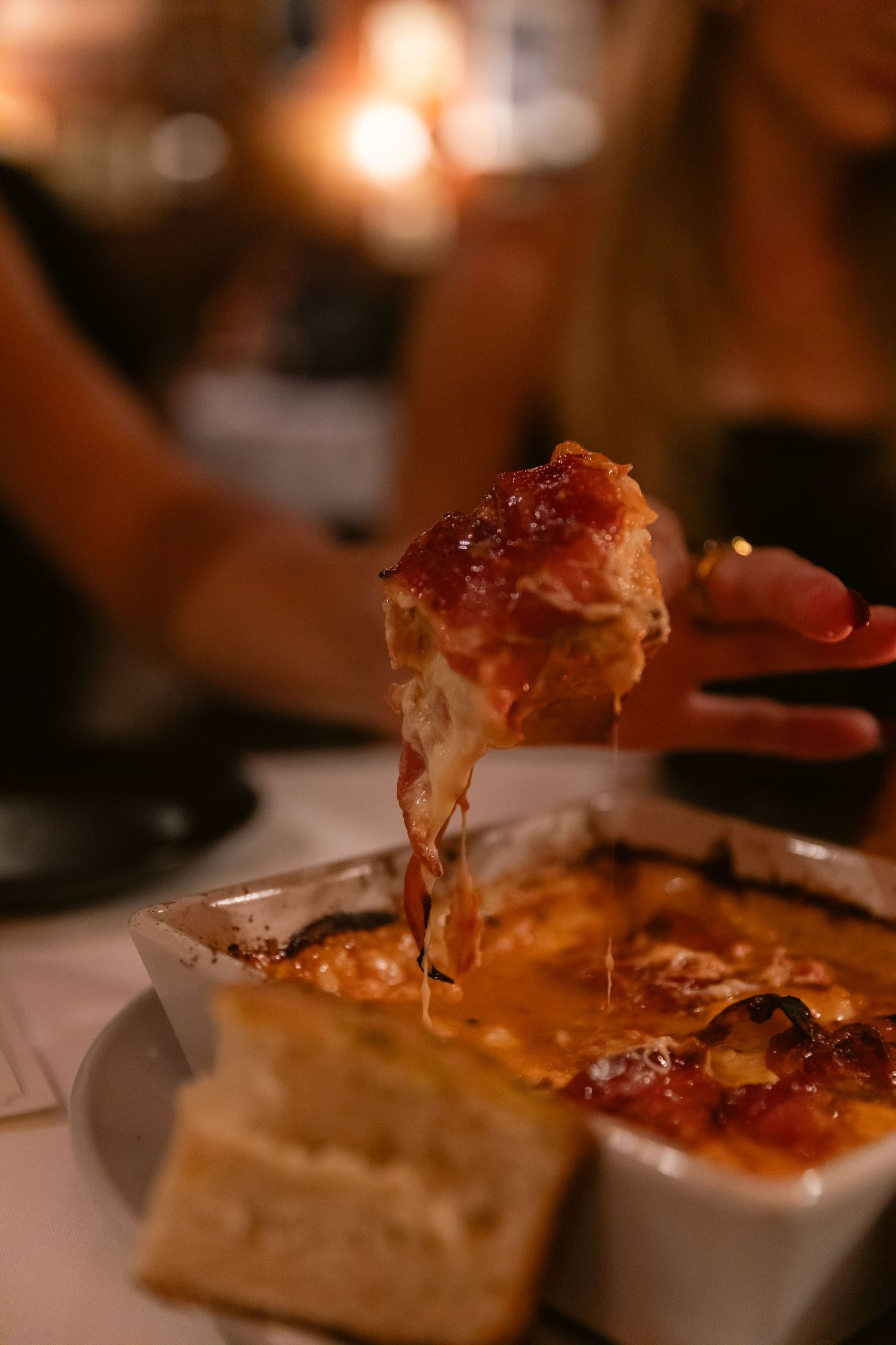 Close-up of melted cheese being pulled from a baked dish in warm lighting.