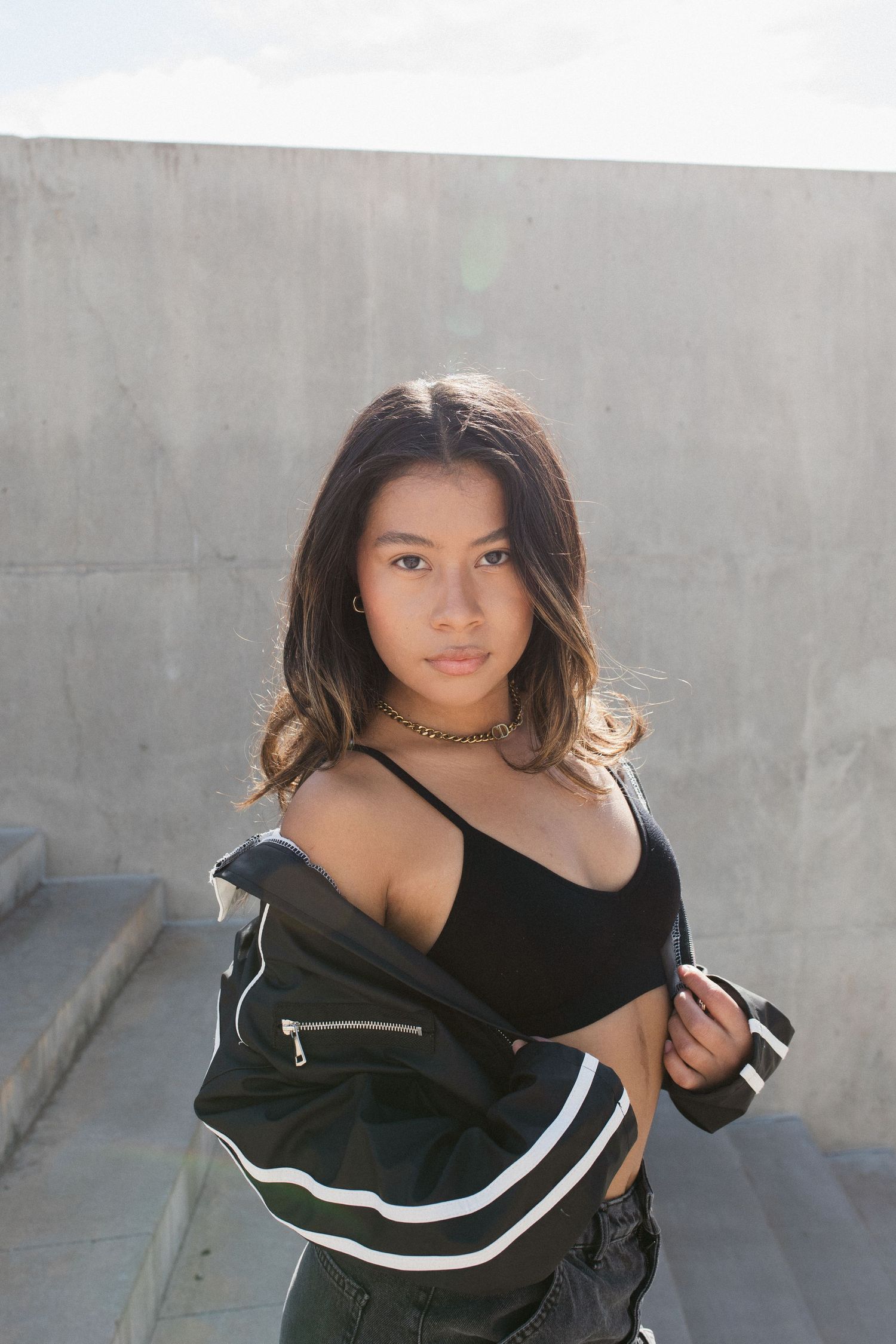 A series of fashion photos showing a black off-shoulder top with white stripe detail against a concrete wall backdrop.