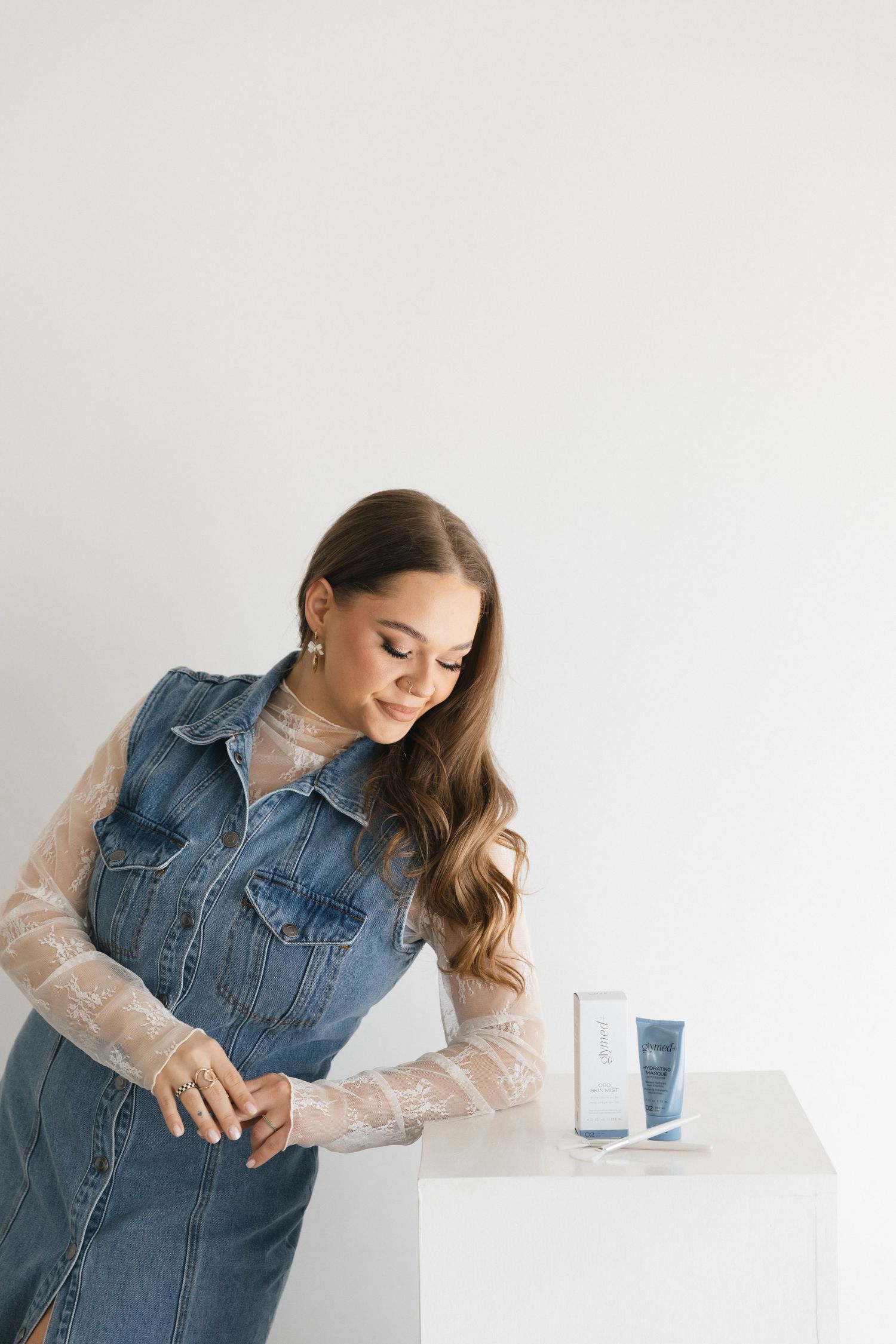 Person in denim vest with sheer sleeves poses gracefully against white background in elegant studio portraits.