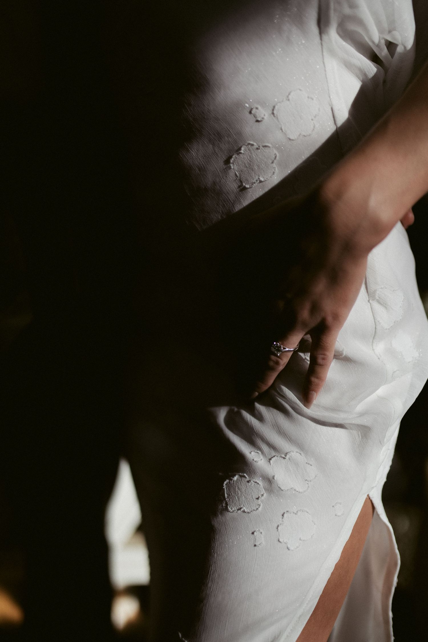 Close-up of hands against white lace wedding dress fabric showing delicate details and texture.
