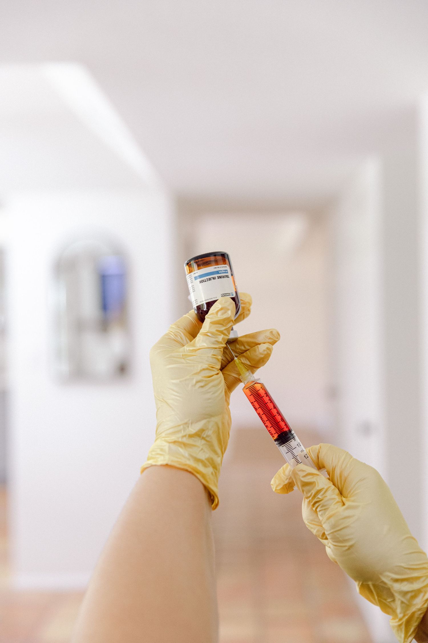 Gloved hands preparing medical vials and syringes against a white background.