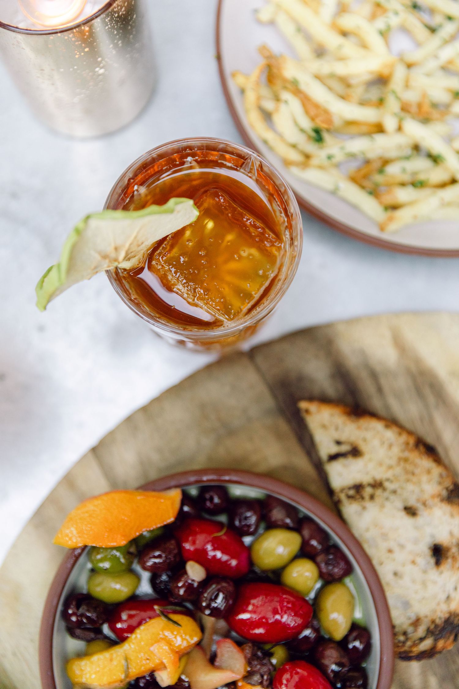 Overhead view of mixed olives, cocktail and french fries on a marble surface.