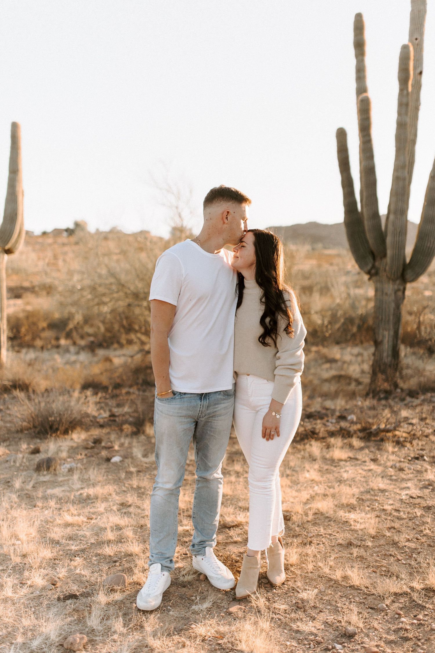 A romantic couple embraces among towering saguaro cacti in the Arizona desert.