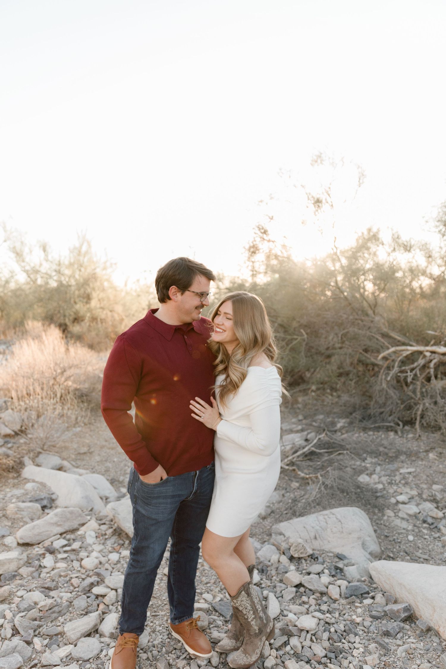Couple embraces on rocky desert terrain during golden hour photoshoot.