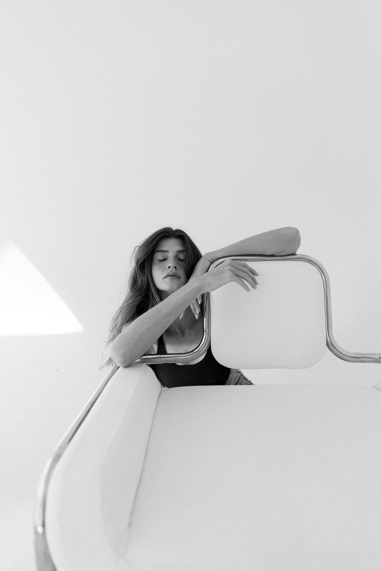 Black and white photo of a woman leaning over a modern white railing with chrome accents in a minimalist setting.