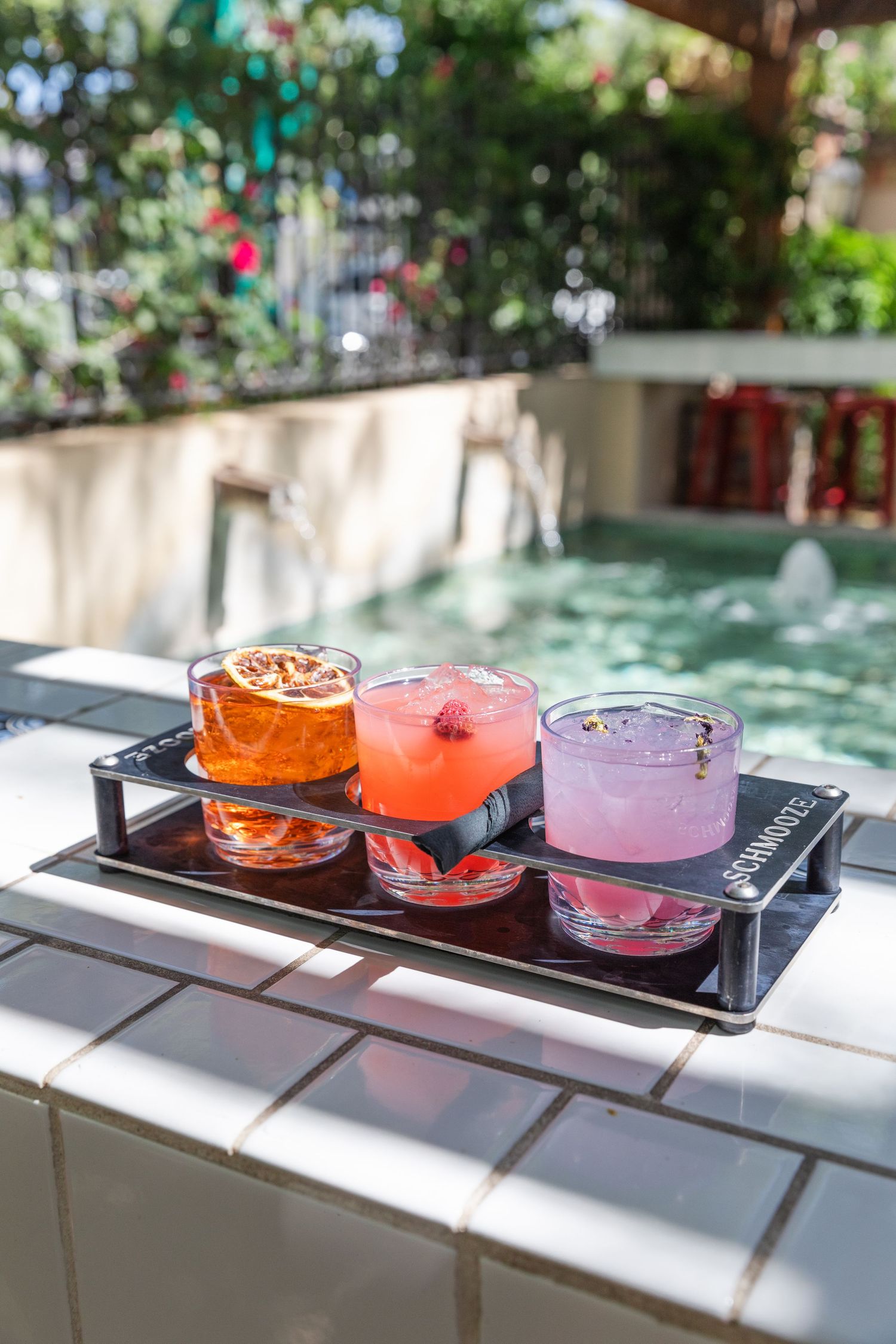 Colorful cocktail flight served on black tray outdoors by pool.