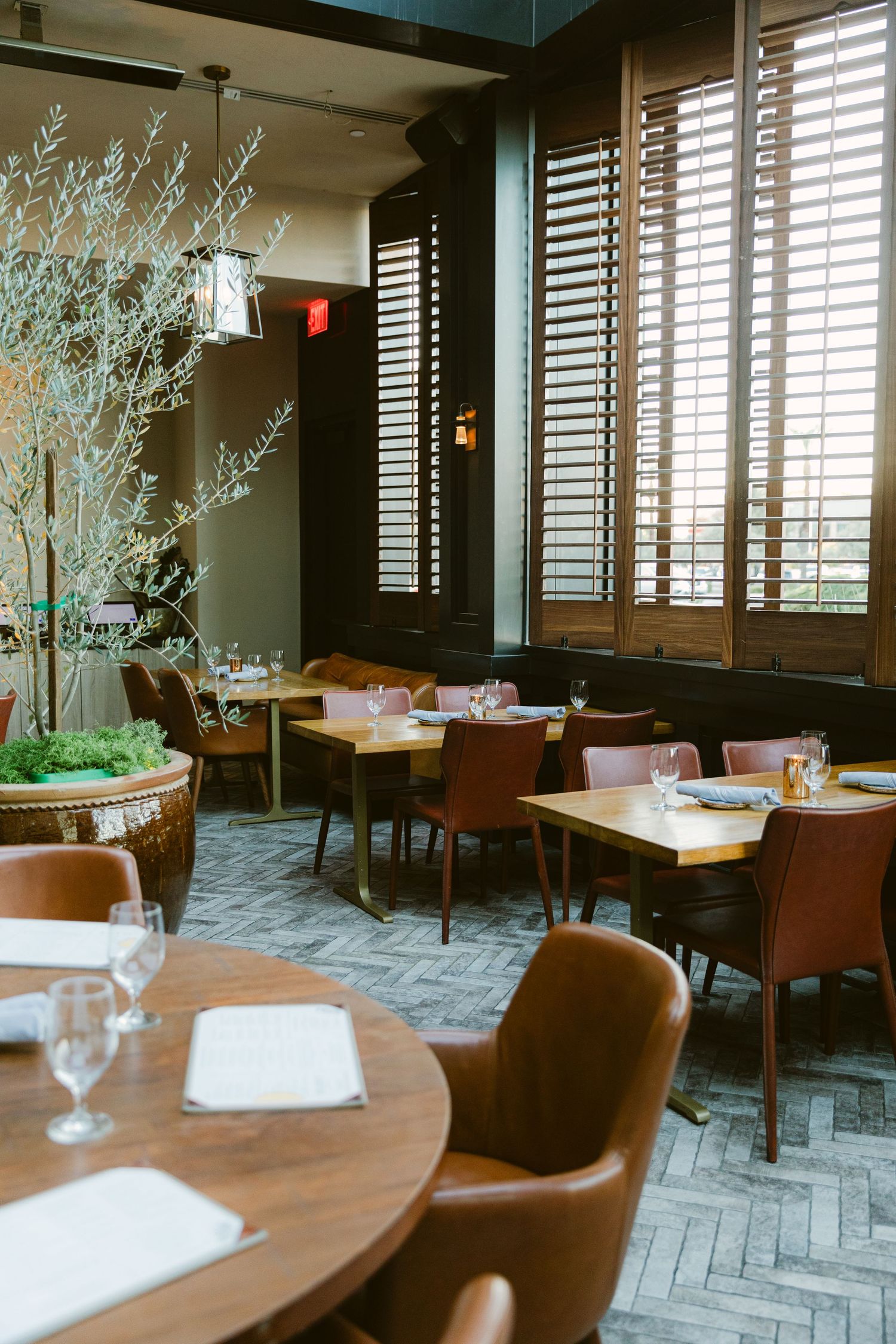 Elegant restaurant interior with wood shutters, round tables and modern floral arrangements.