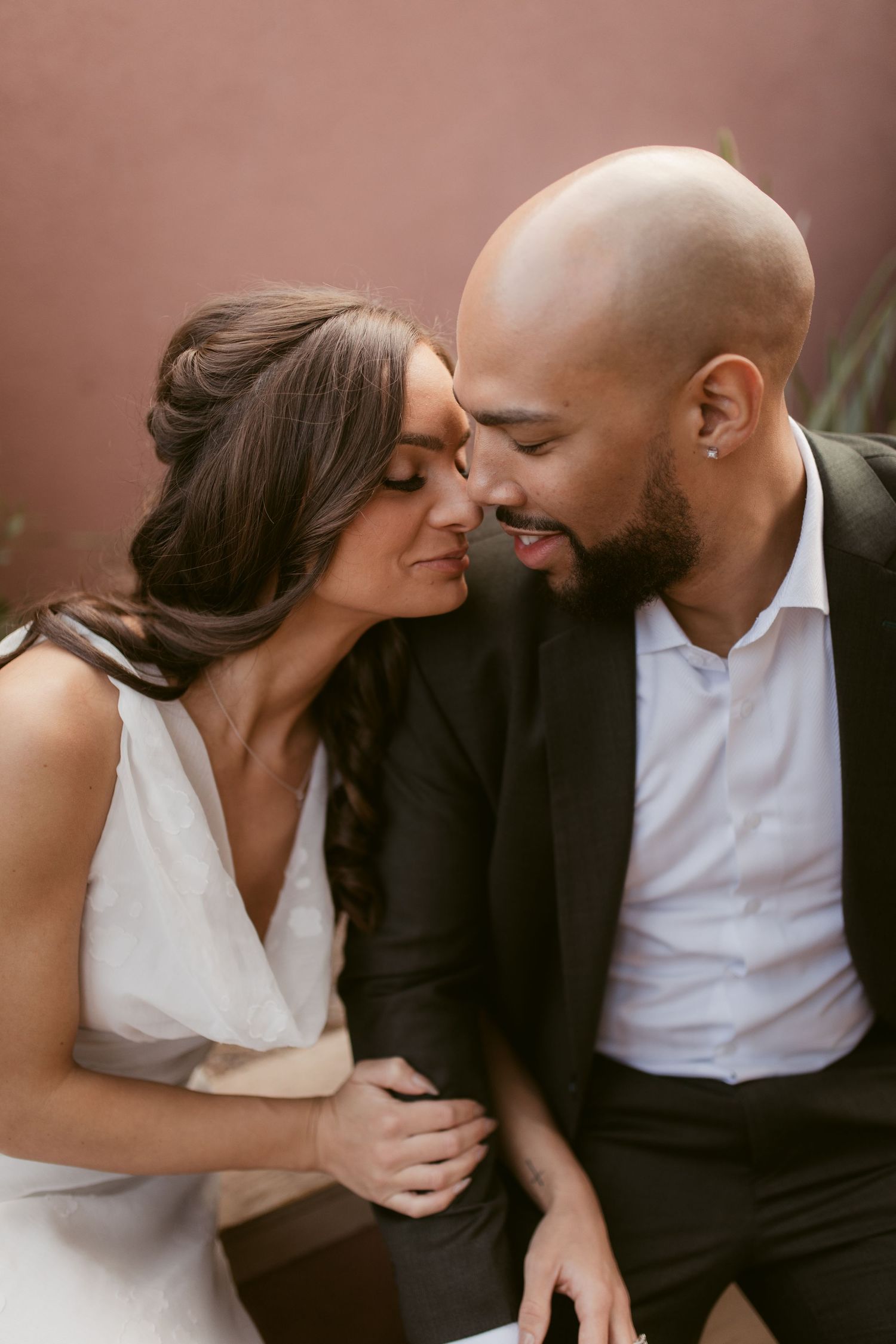 A romantic moment between a couple in wedding attire against a terracotta colored wall.