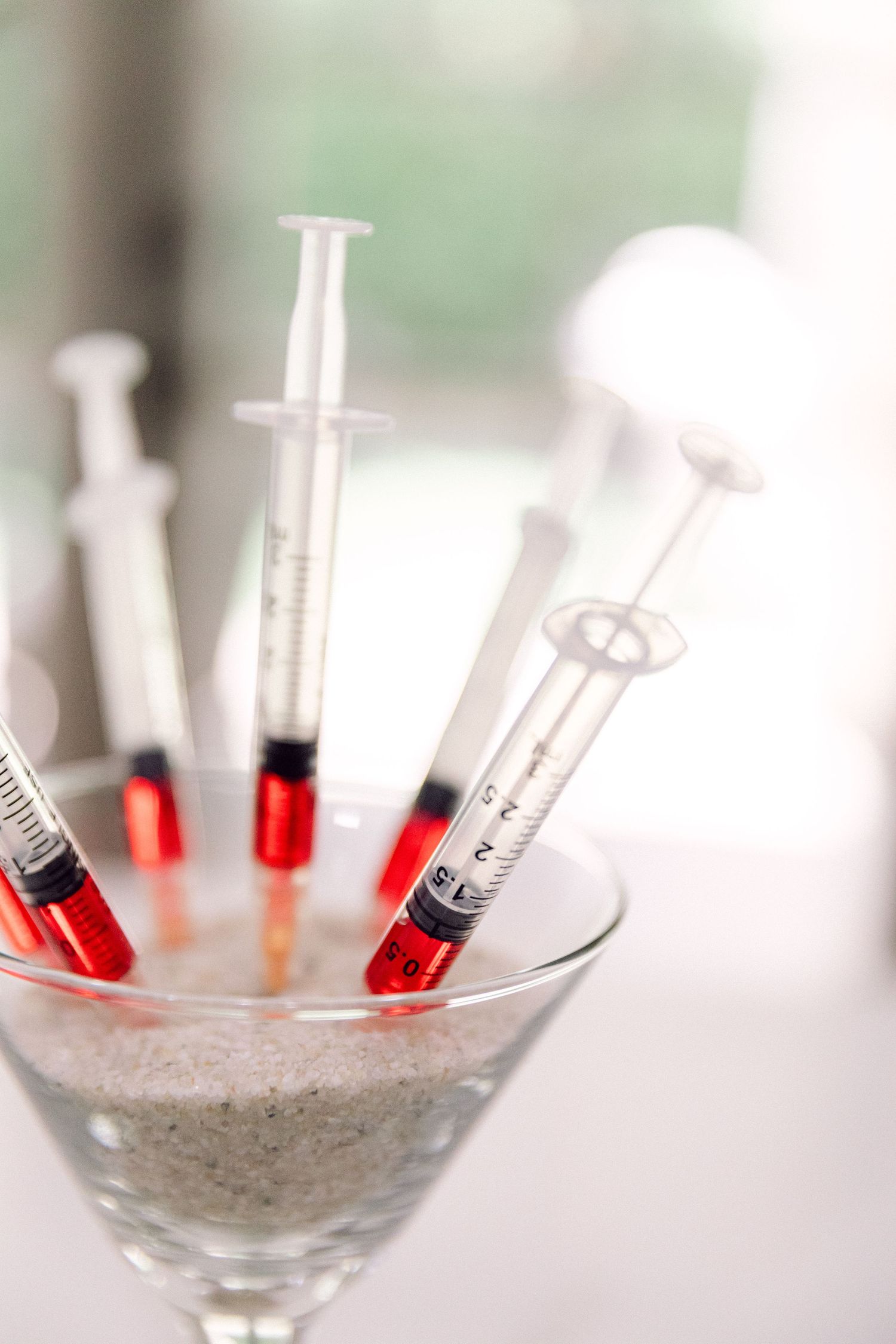 Red-tipped syringes arranged artistically in a martini glass with sand.