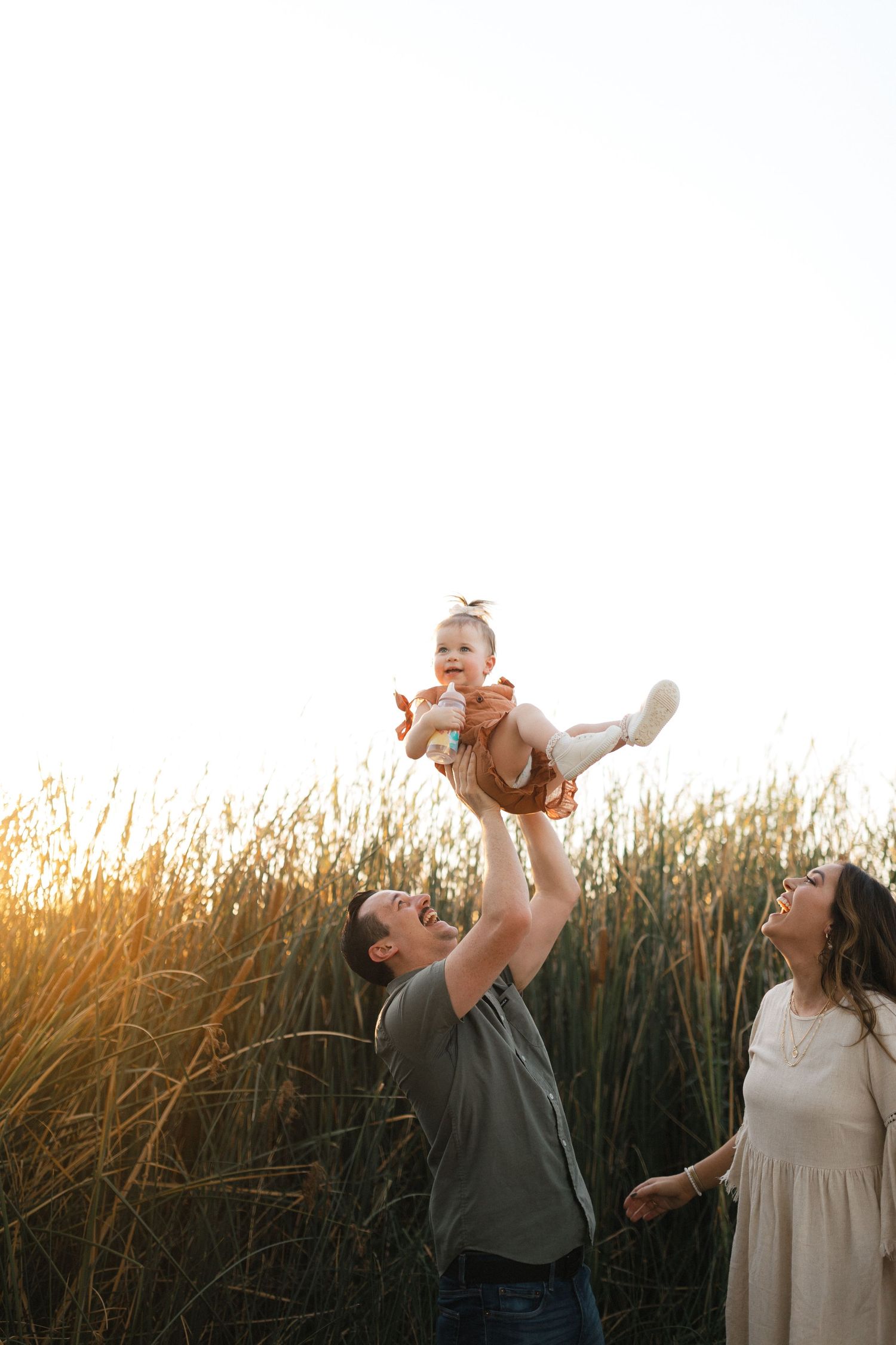 Family playing and having fun together while laughing in a wheat field at golden sunset.