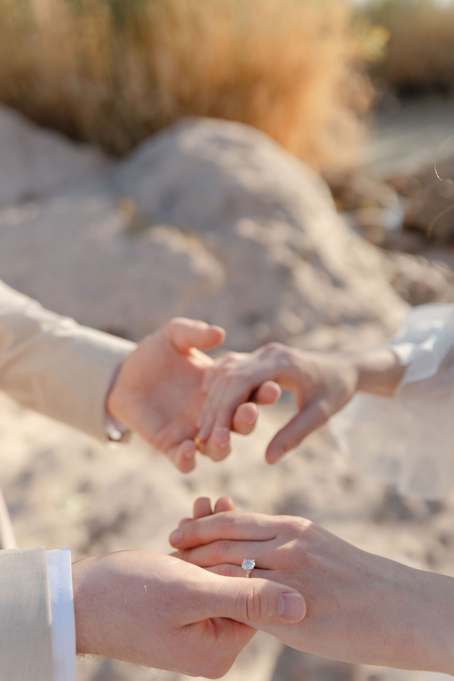 Close-up sequence showing a diamond engagement ring being placed on a hand against a sandy background.