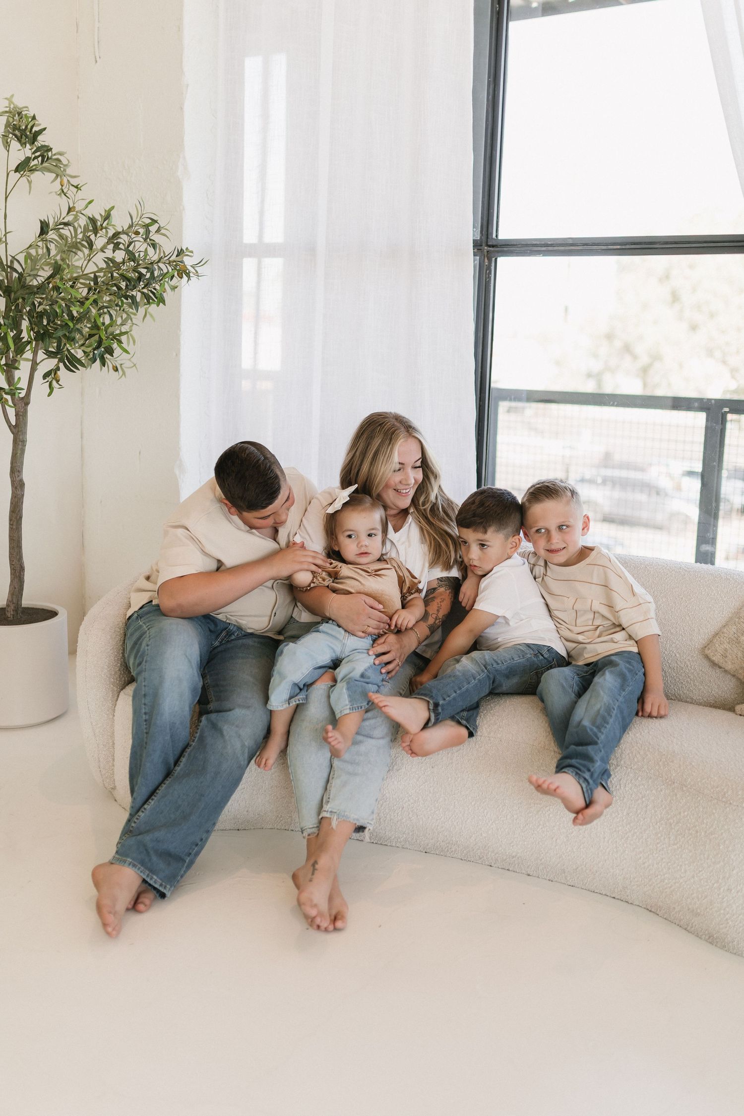Group poses while sitting on a white couch in matching blue denim and white outfits in a bright, modern space.