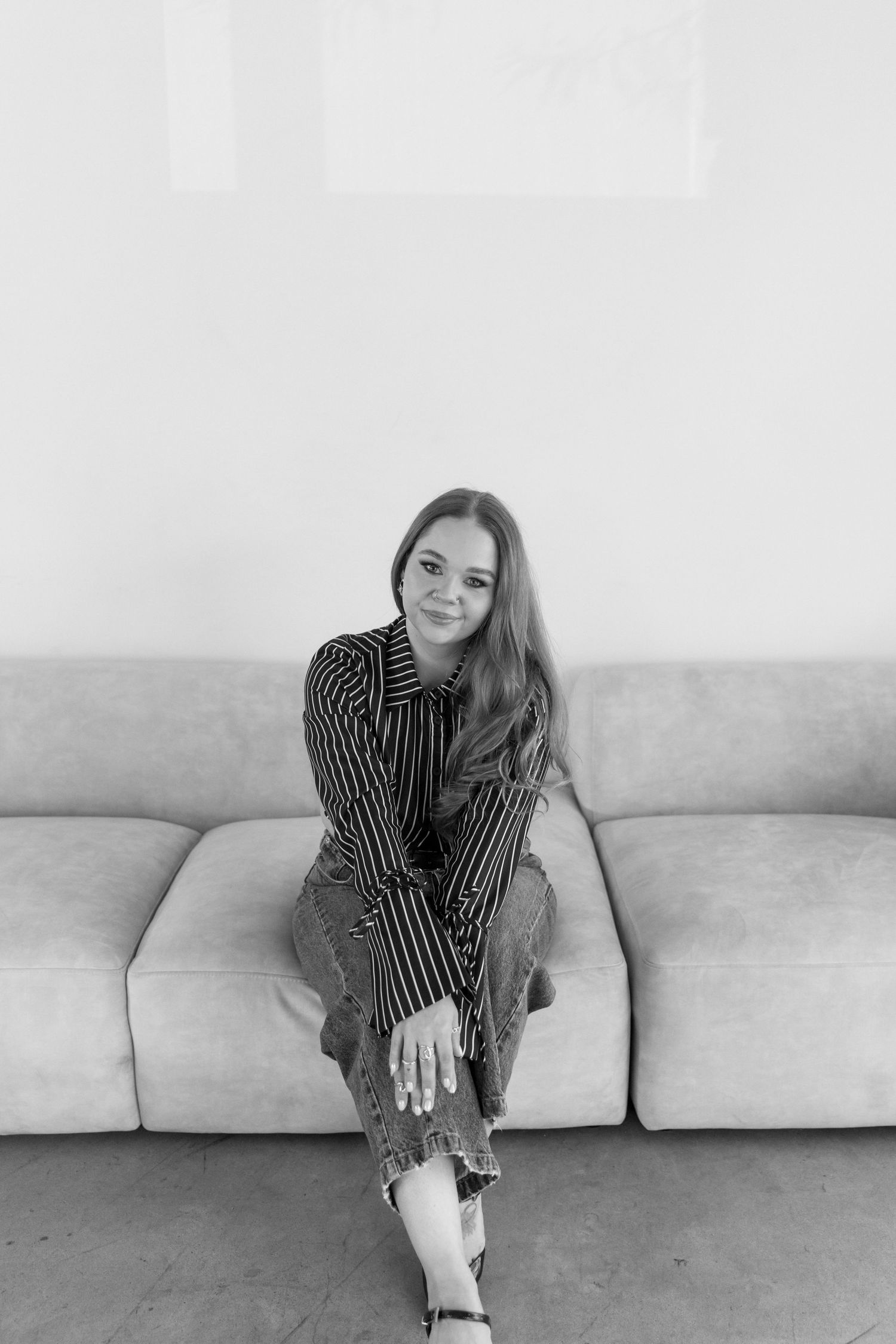 Black and white portrait of someone in a striped shirt sitting casually on a light colored sofa.