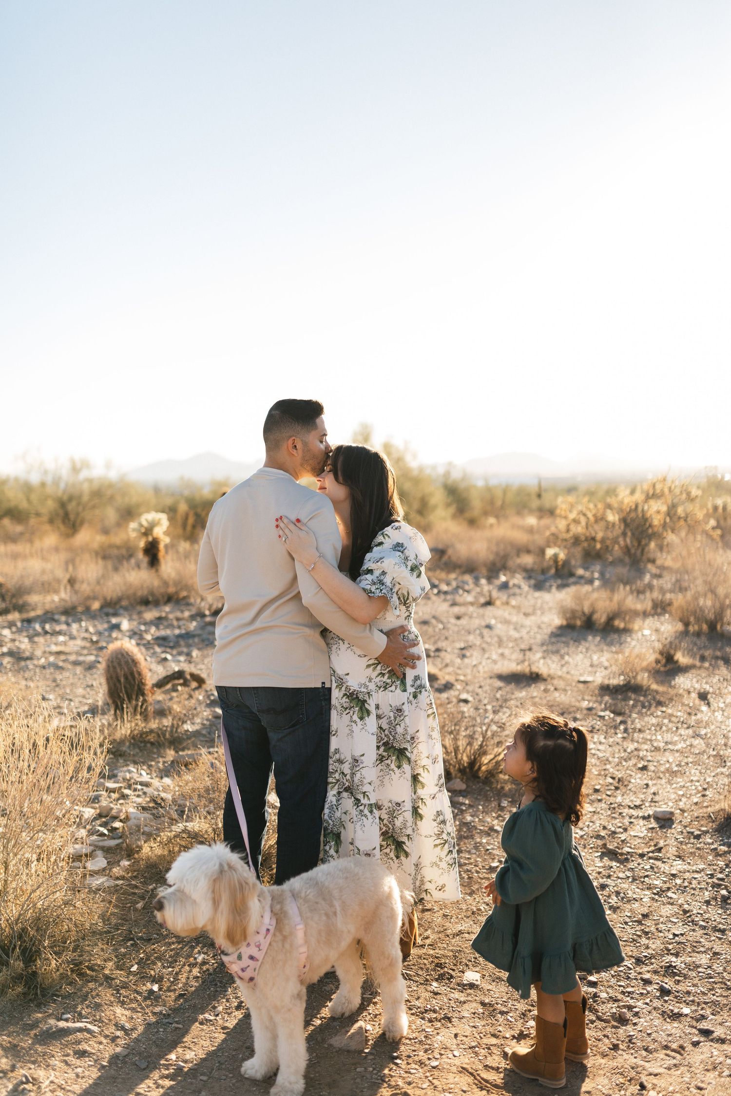 Family spending time together with their fluffy goldendoodle dog in a desert landscape at sunset.