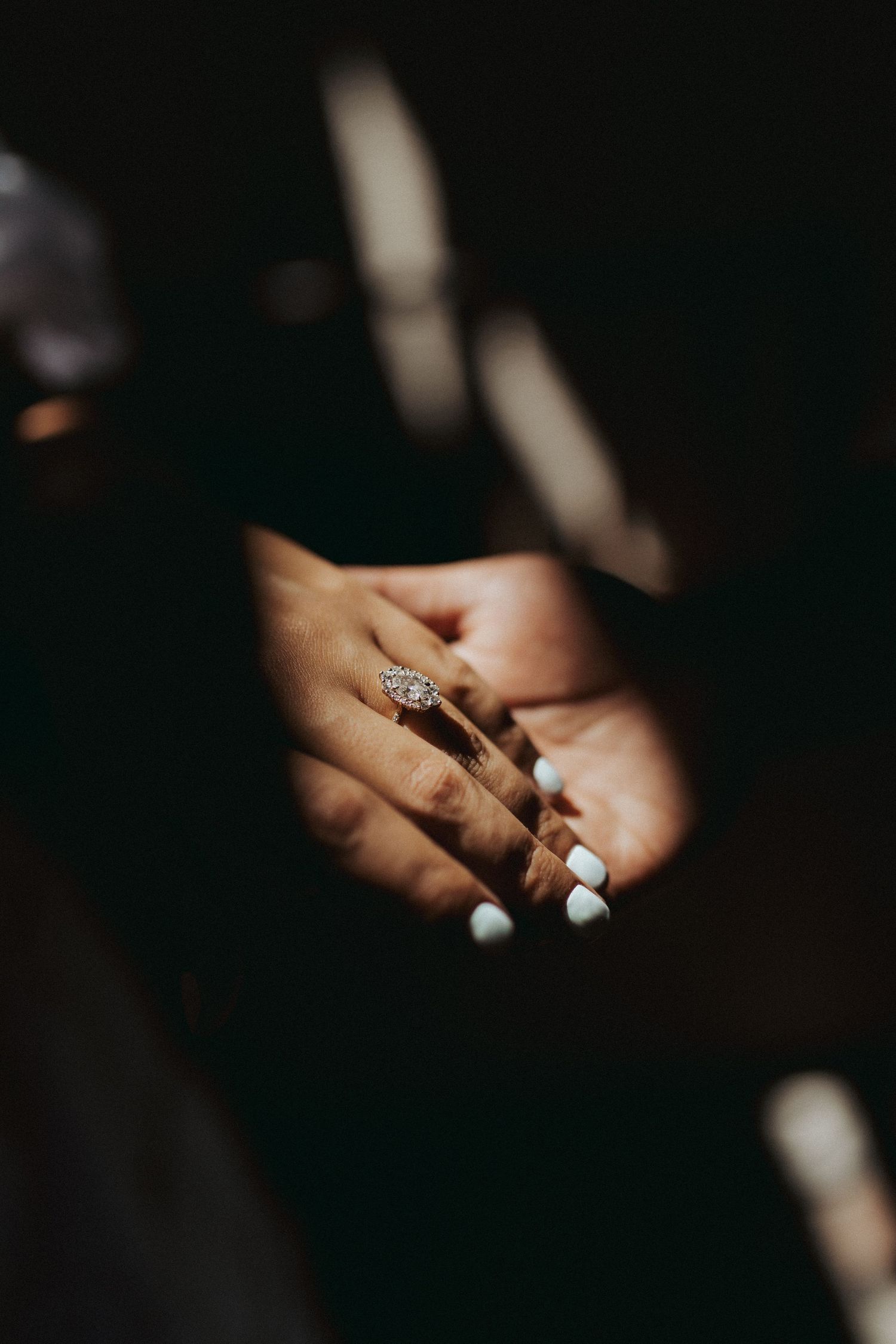 Close-up of hands showing engagement ring with white nail polish.