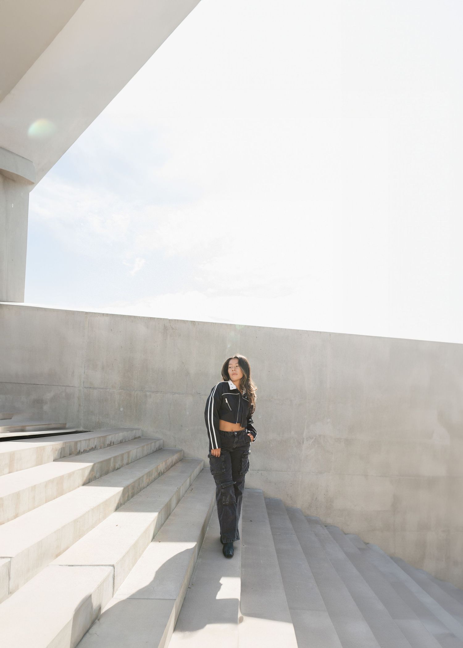 Figure walking up a curved concrete staircase with minimalist architectural design and dramatic shadows.