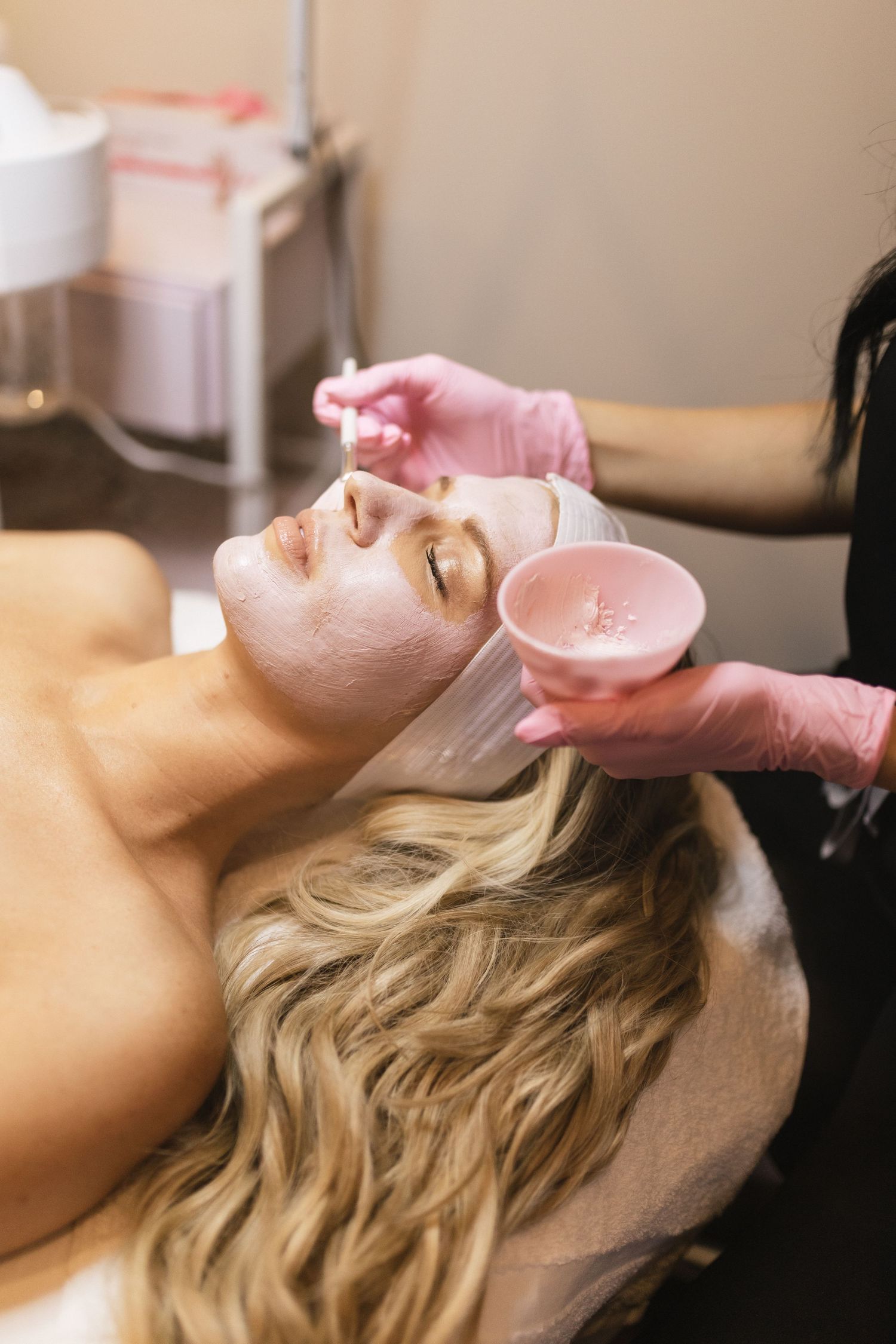 A person lying back receiving a professional facial treatment with eye pads and skincare application.