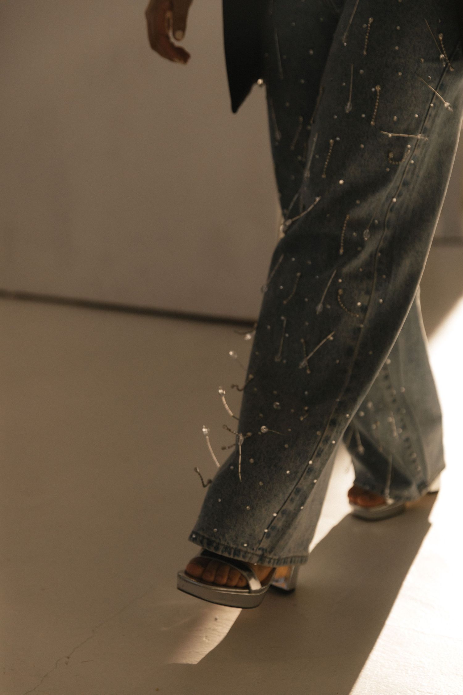 Multiple pairs of legs wearing blue jeans and brown shoes walking in a line on a reflective floor surface.