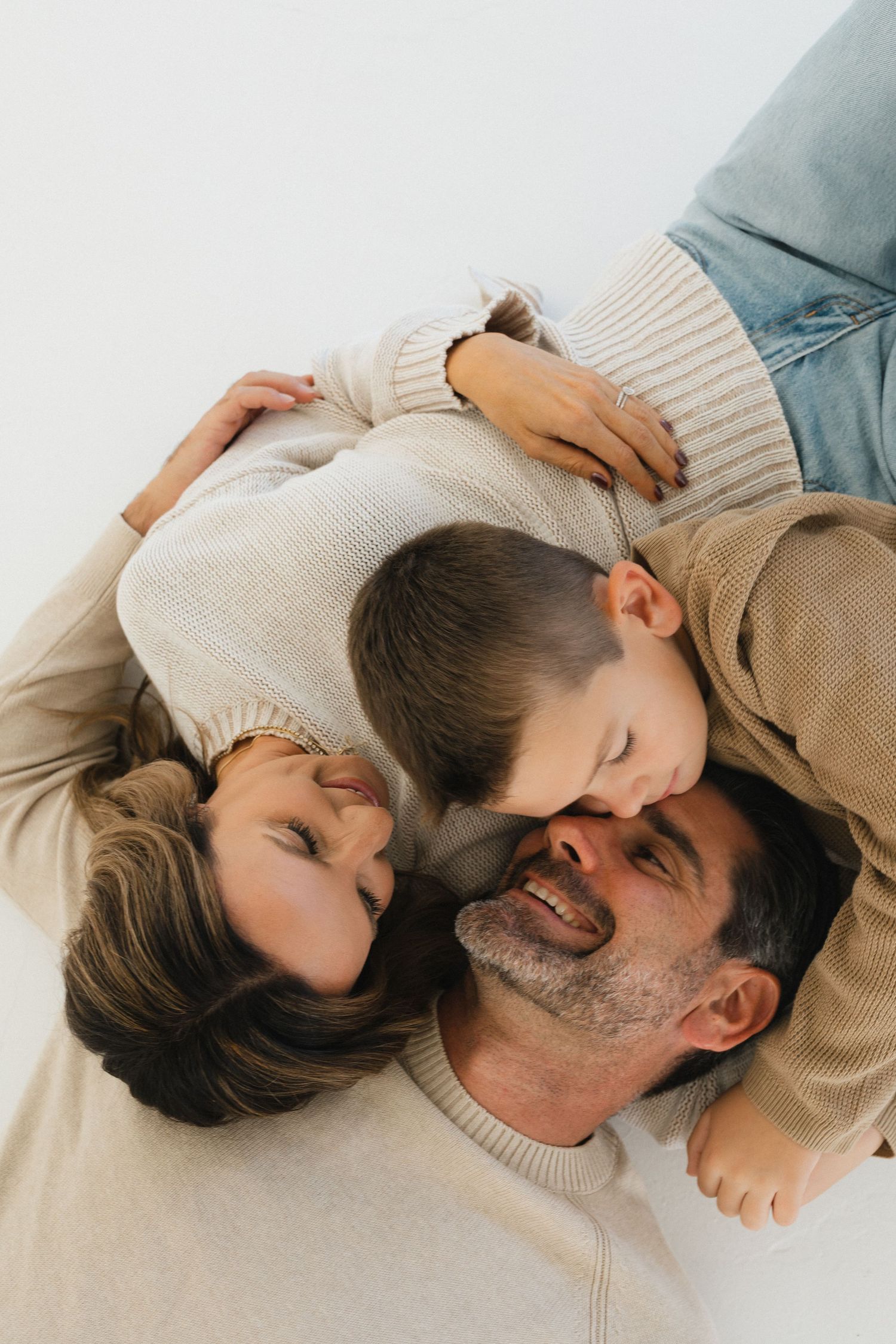 A parent and child lying down together in cream colored sweaters sharing an intimate moment of connection.