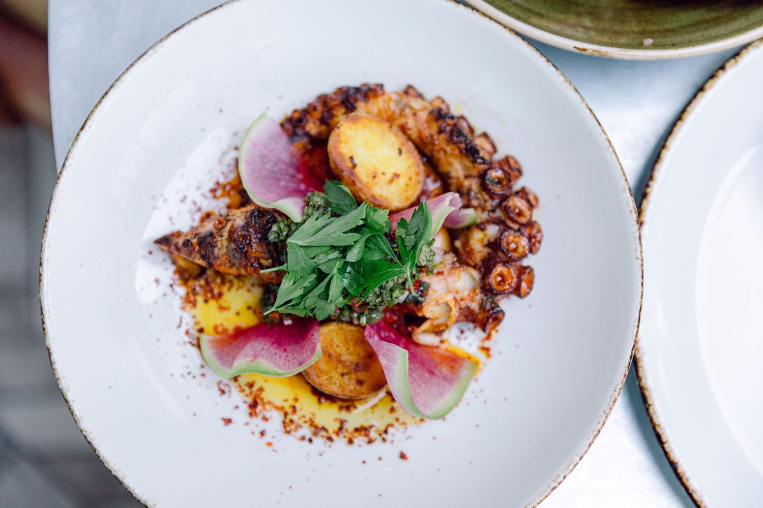 Gourmet dish featuring roasted potatoes, fresh herbs, and edible flowers arranged artfully on a white plate.