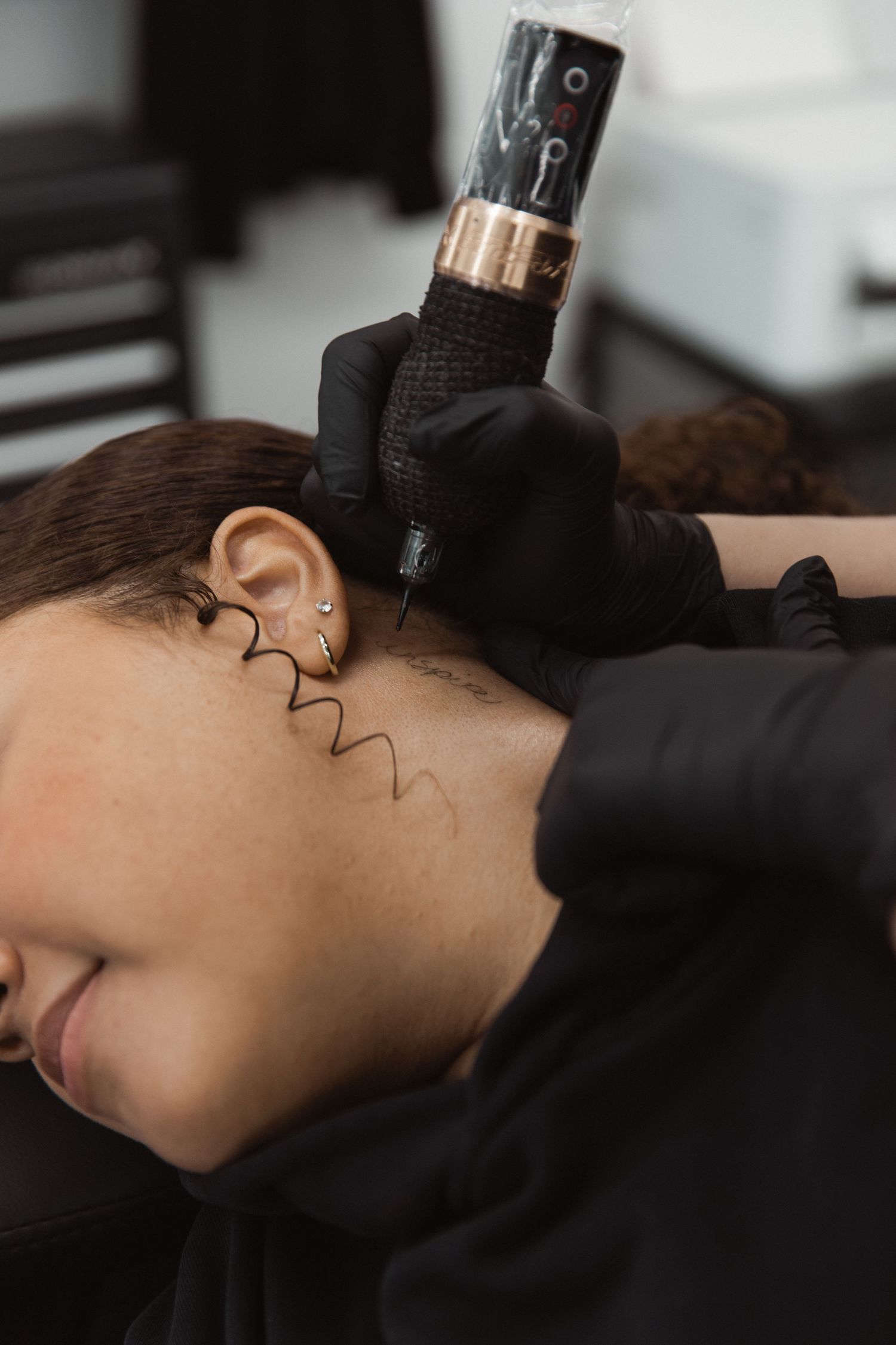 Close-up of tattoo machine creating design near client's ear.