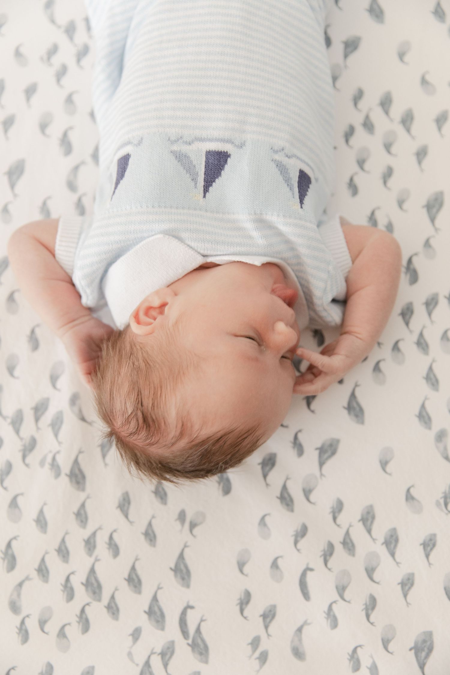 Sleeping baby wearing blue and white striped outfit lies on patterned bedding.