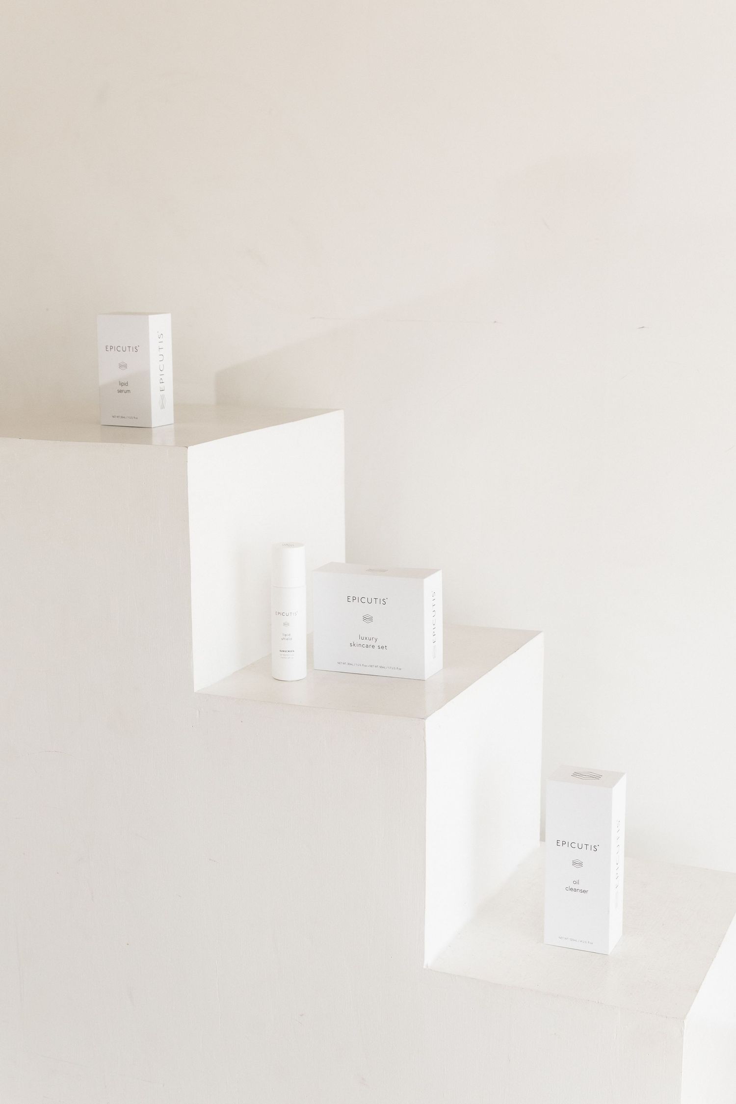 Minimalist white skincare product containers arranged on descending white steps against a light neutral background.