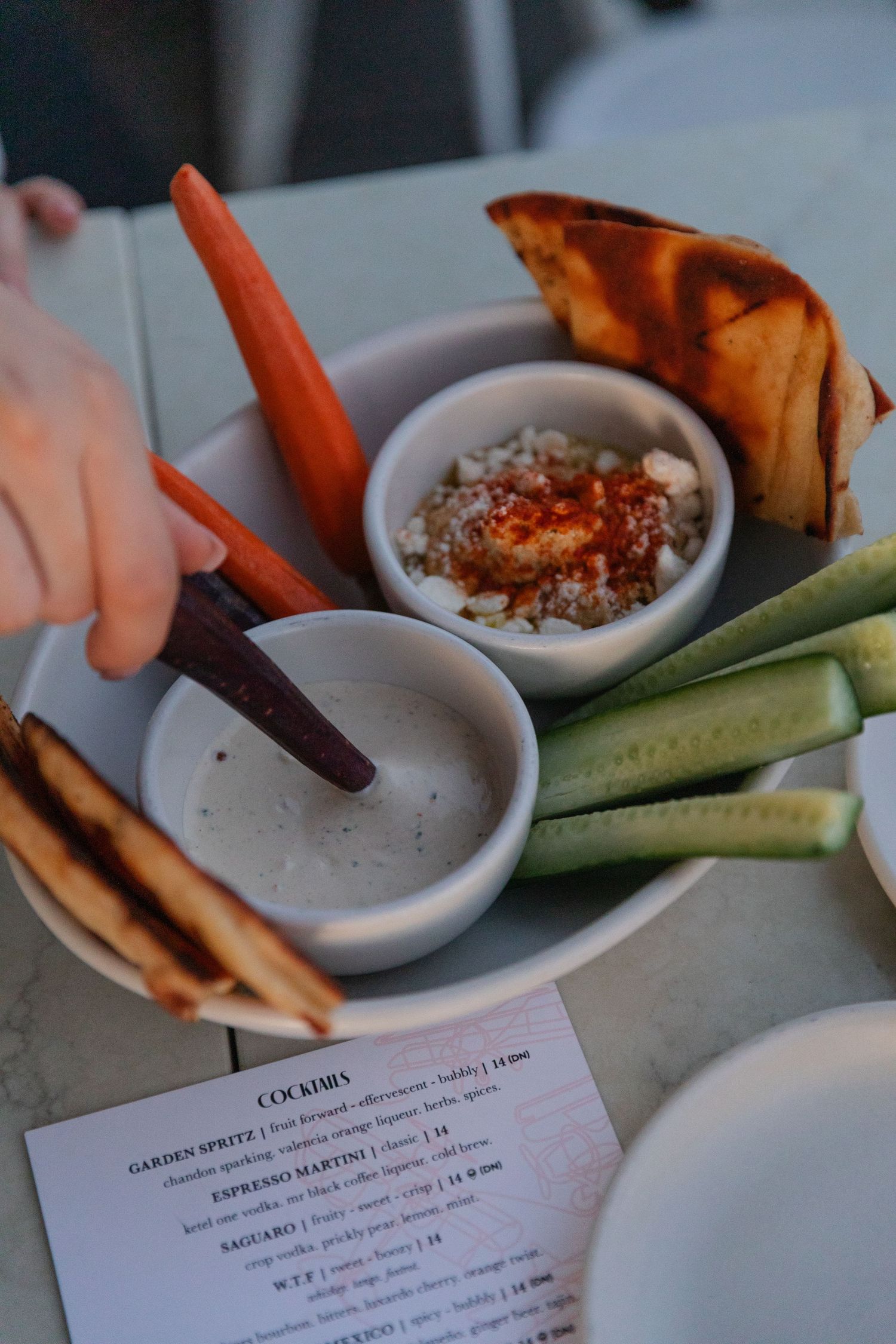 Fresh vegetable crudites and dipping sauces served with menu on a white plate.