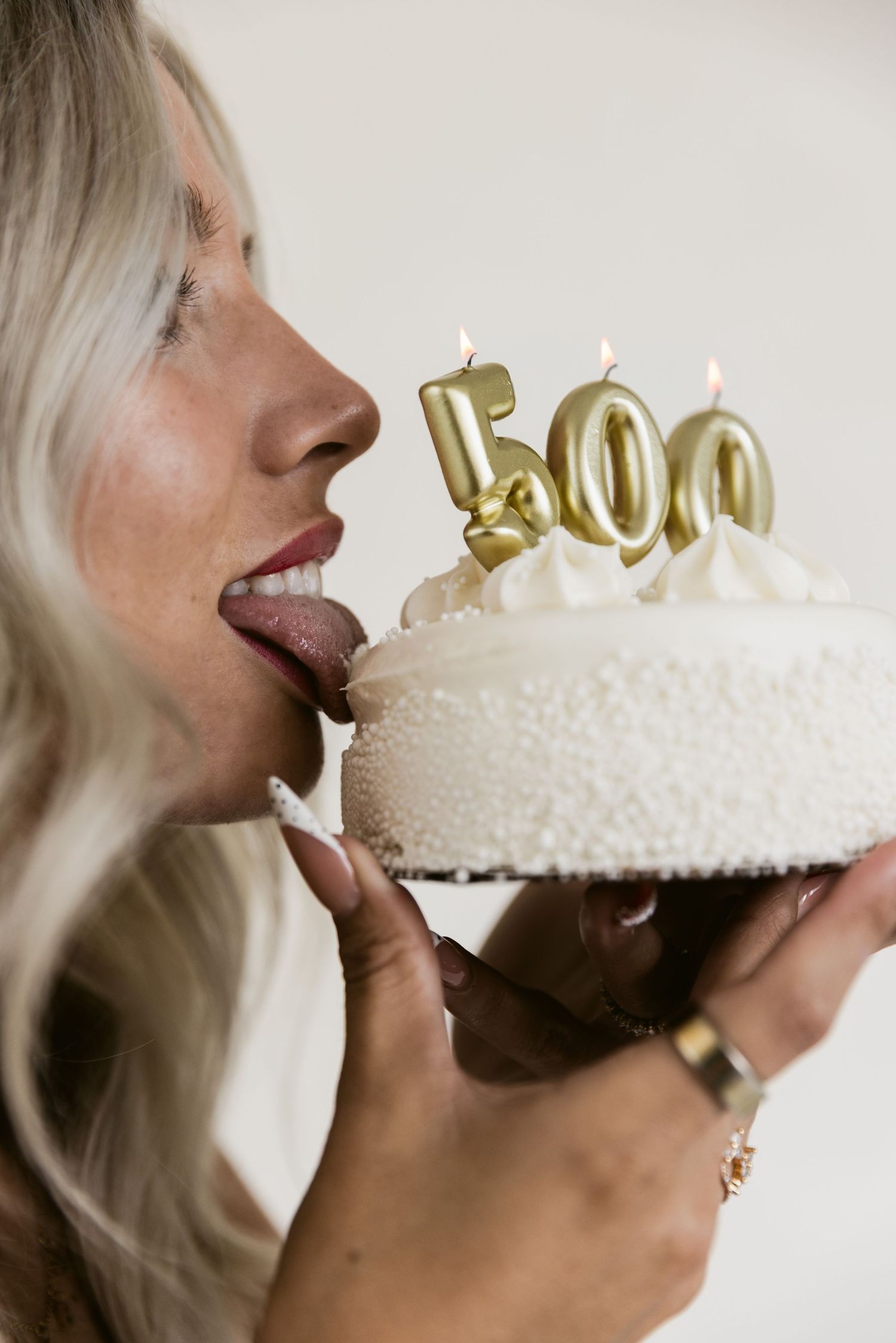 Woman licking a white cake with gold number 500 candles, celebrating a milestone birthday.
