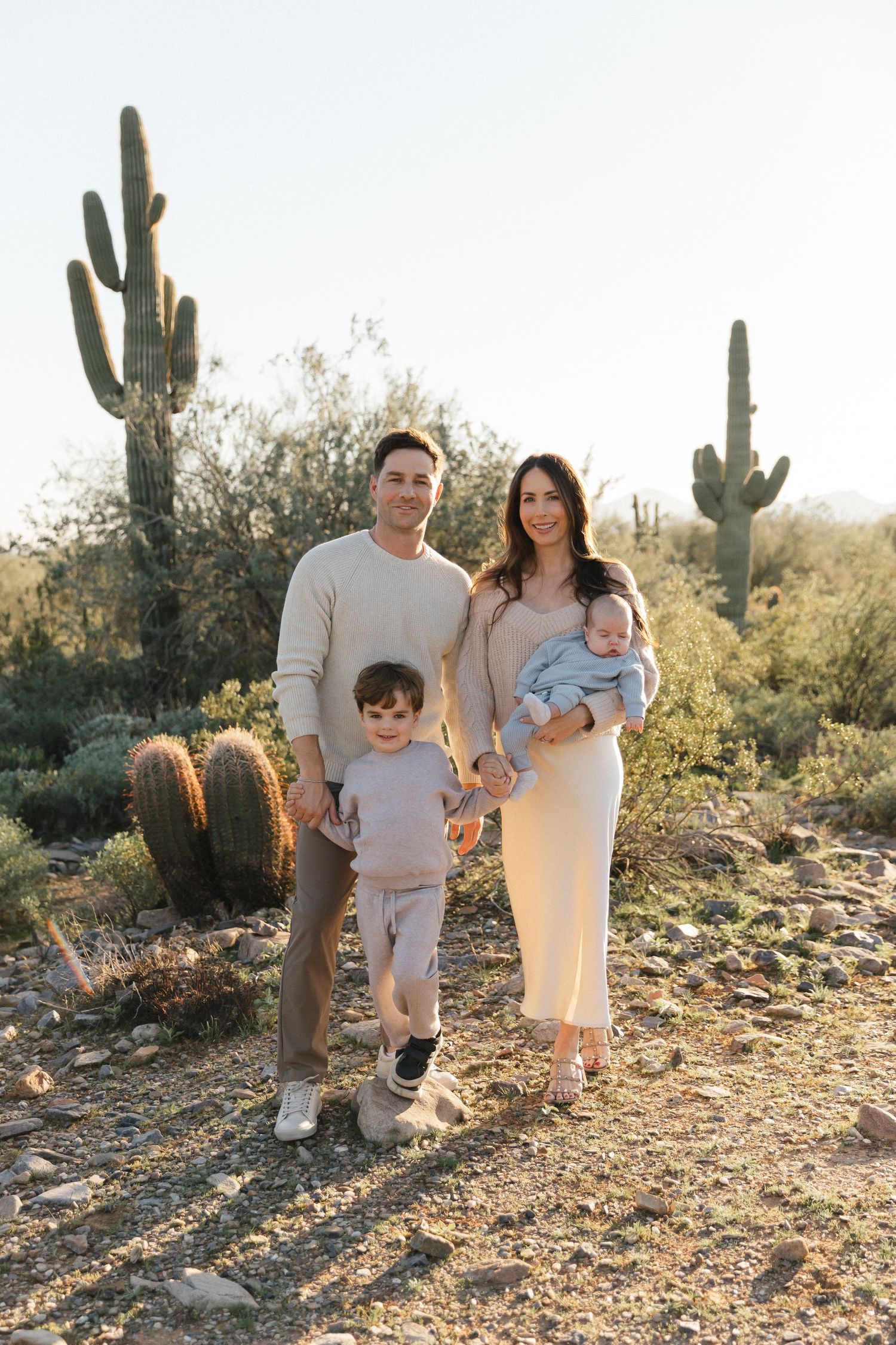 A family poses together in a desert landscape with saguaro cacti and golden sunlight during sunset.