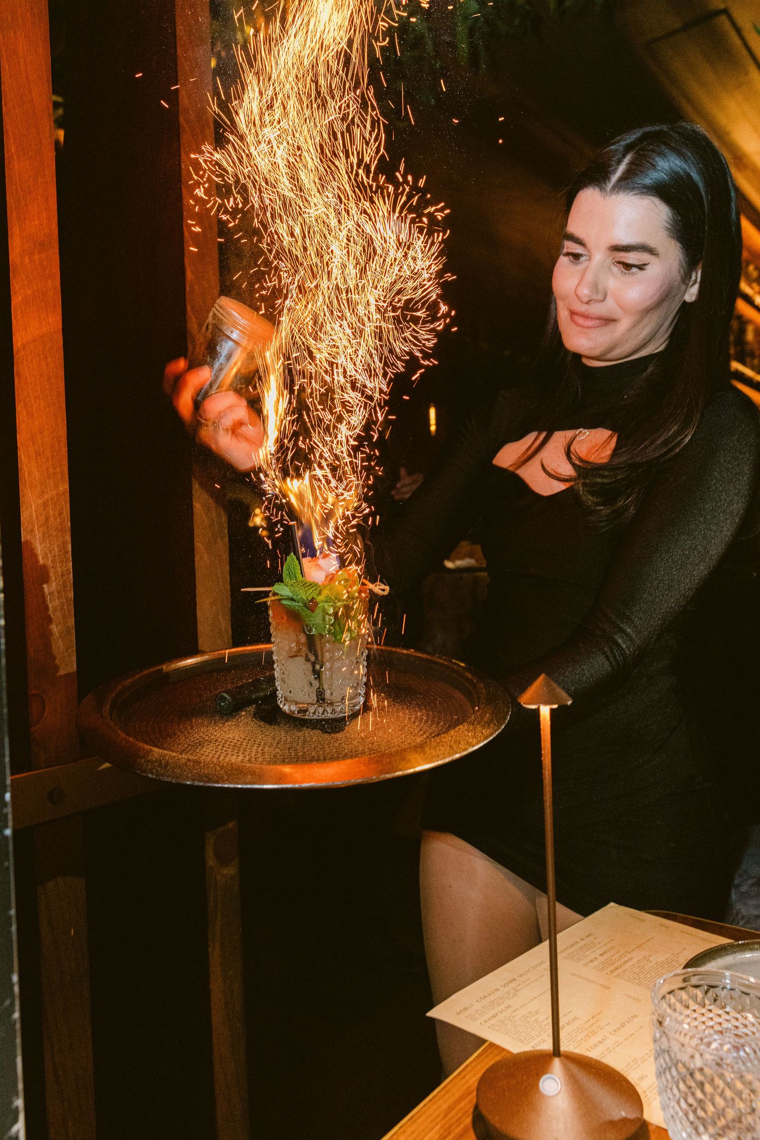 Dramatic flaming cocktail preparation with sparks flying at a restaurant bar.