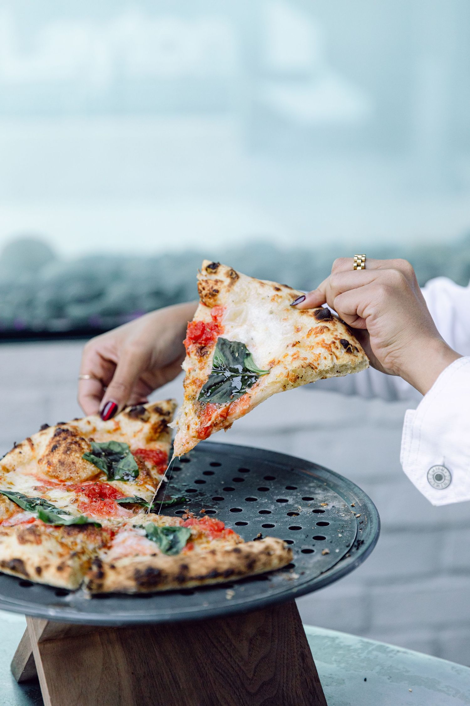 Stretchy cheese pull of a fresh margherita pizza with basil leaves on a dark serving plate.