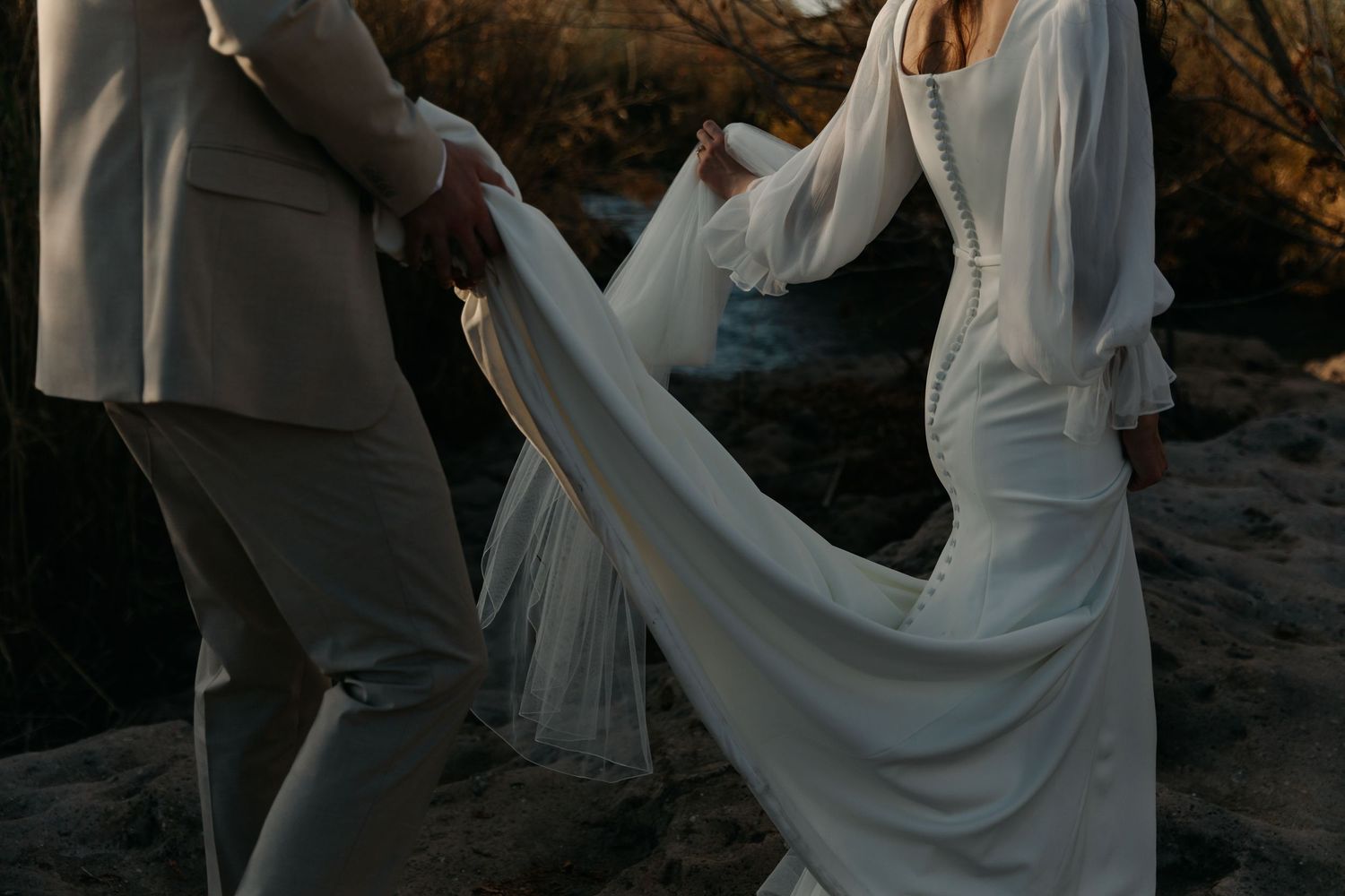 A couple poses together on a rocky beach during sunset for romantic wedding photos.