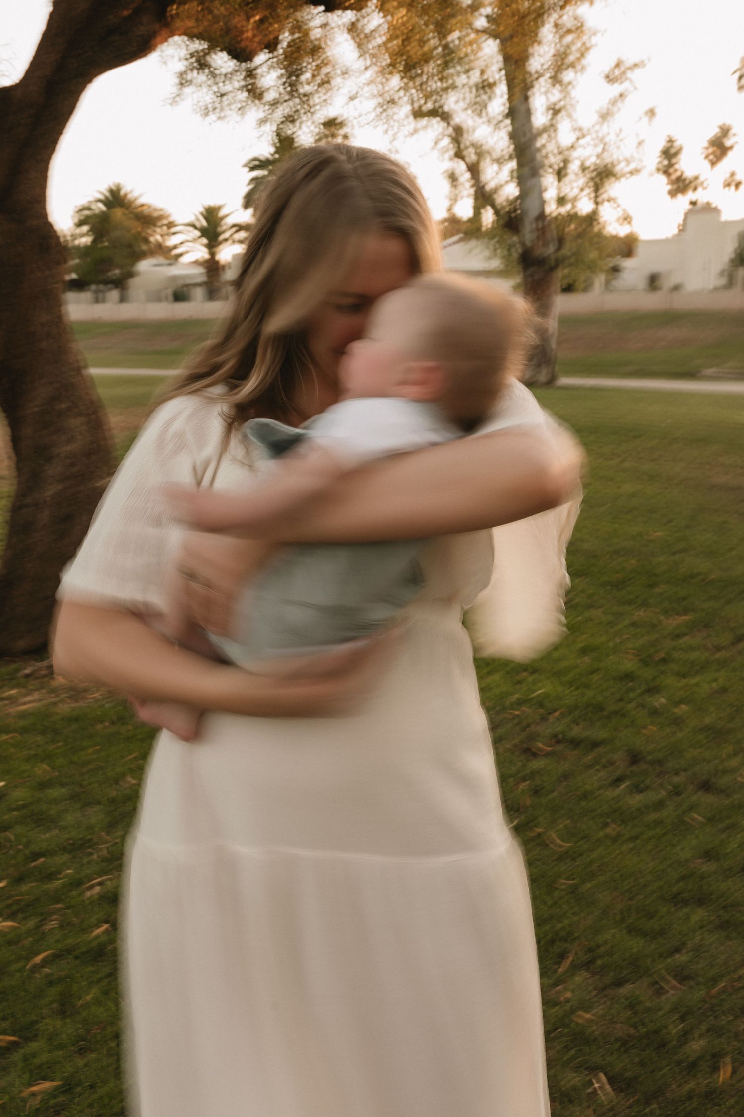 Motion-blurred sequence showing two dancers in white dresses embracing and spinning in a grassy outdoor field at sunset.