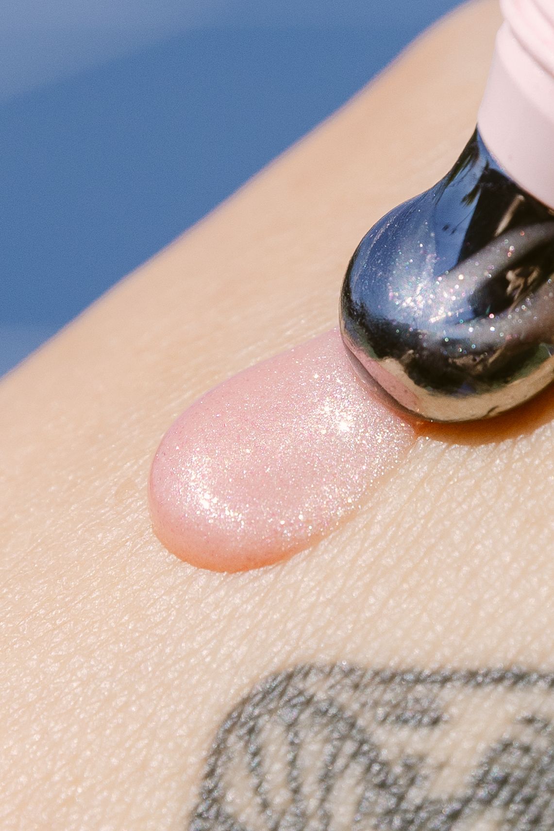 Close-up of a shimmery pink lip gloss swatch on skin next to a glossy black applicator wand.