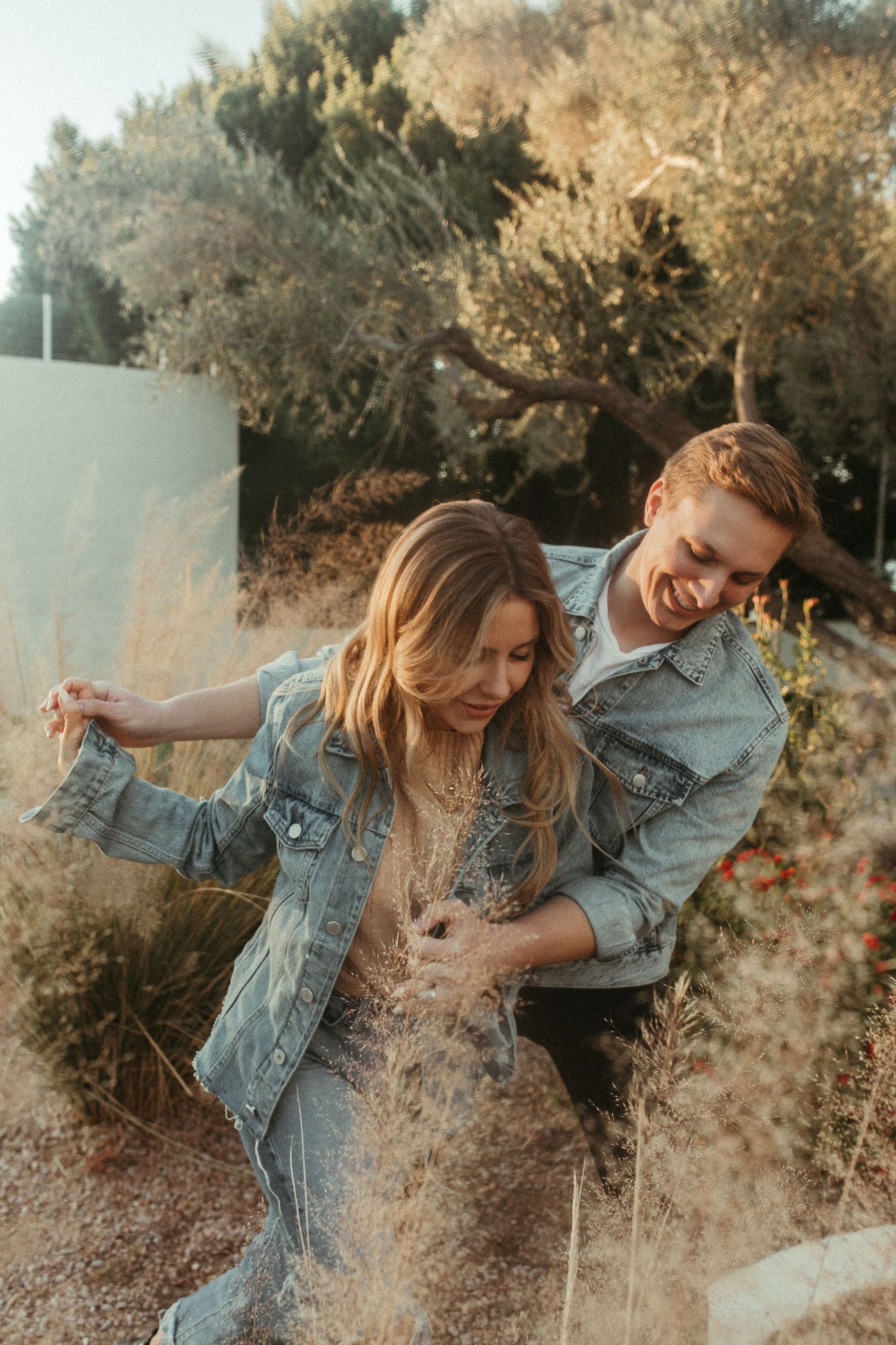 A playful couple in matching denim jackets share a candid moment outdoors at sunset.