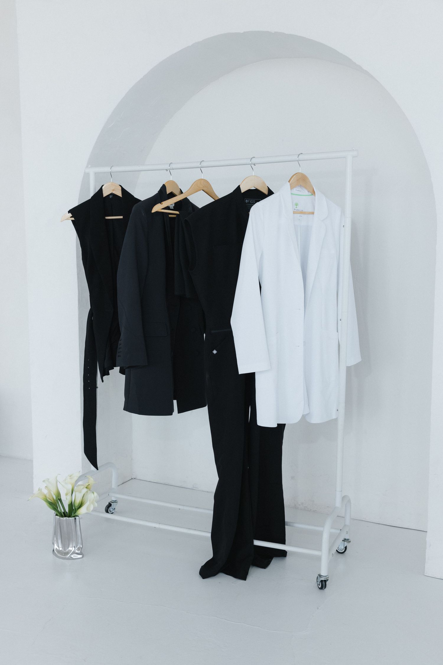 Minimalist clothing rack with black and white garments on wooden hangers against a white arched wall.