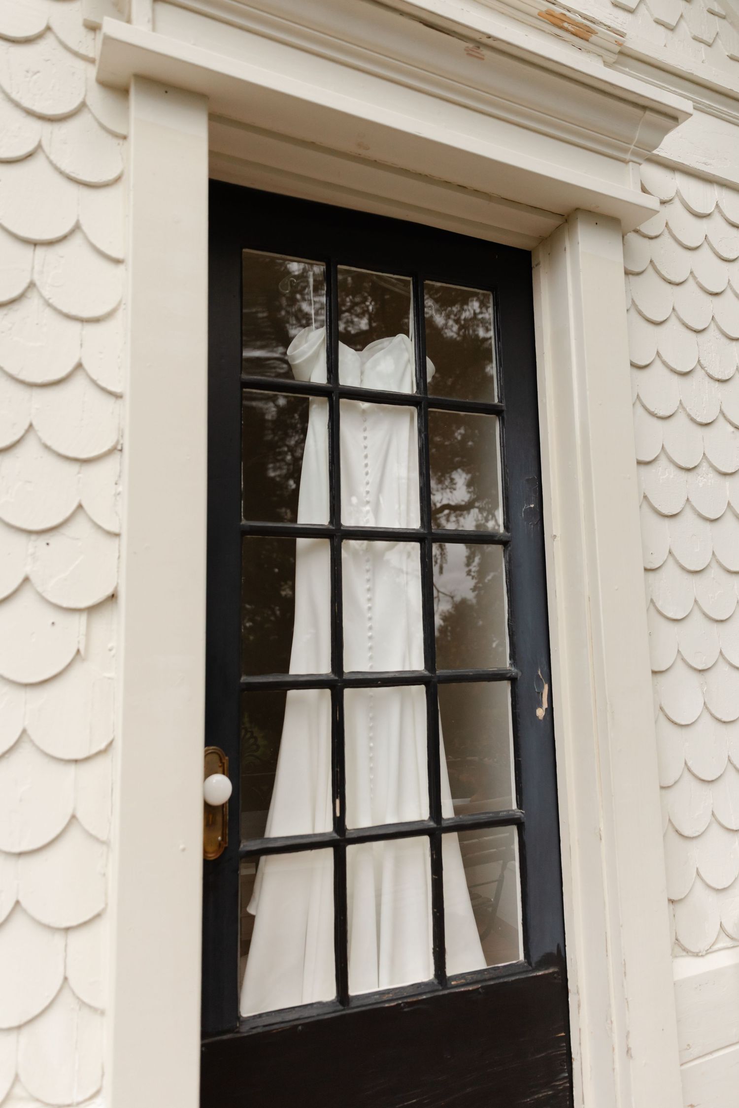 White dress displayed in window with black frame against textured architectural wall with scalloped pattern details.