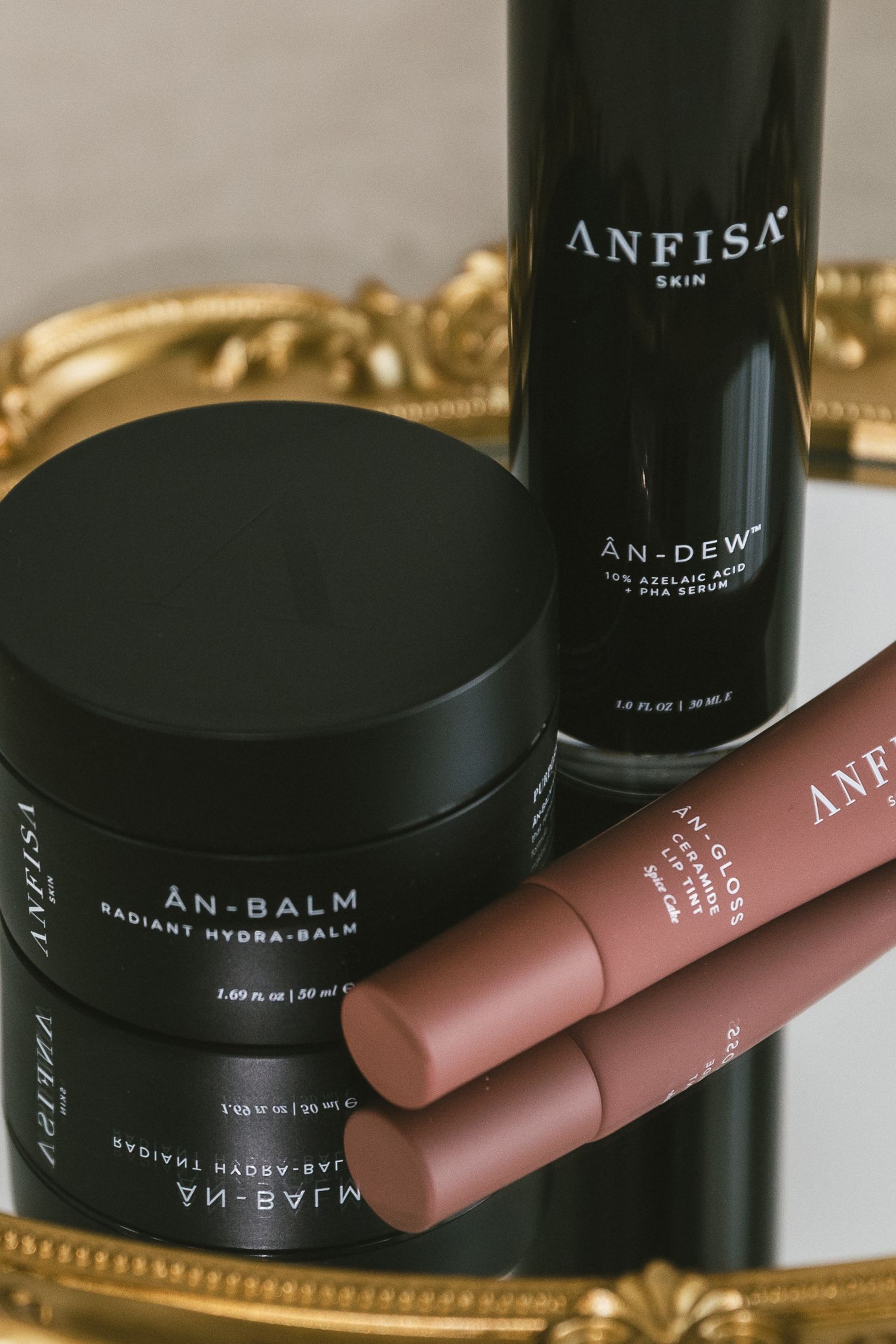 Luxury black skincare product containers and pink lipstick tubes arranged on a reflective gold surface.